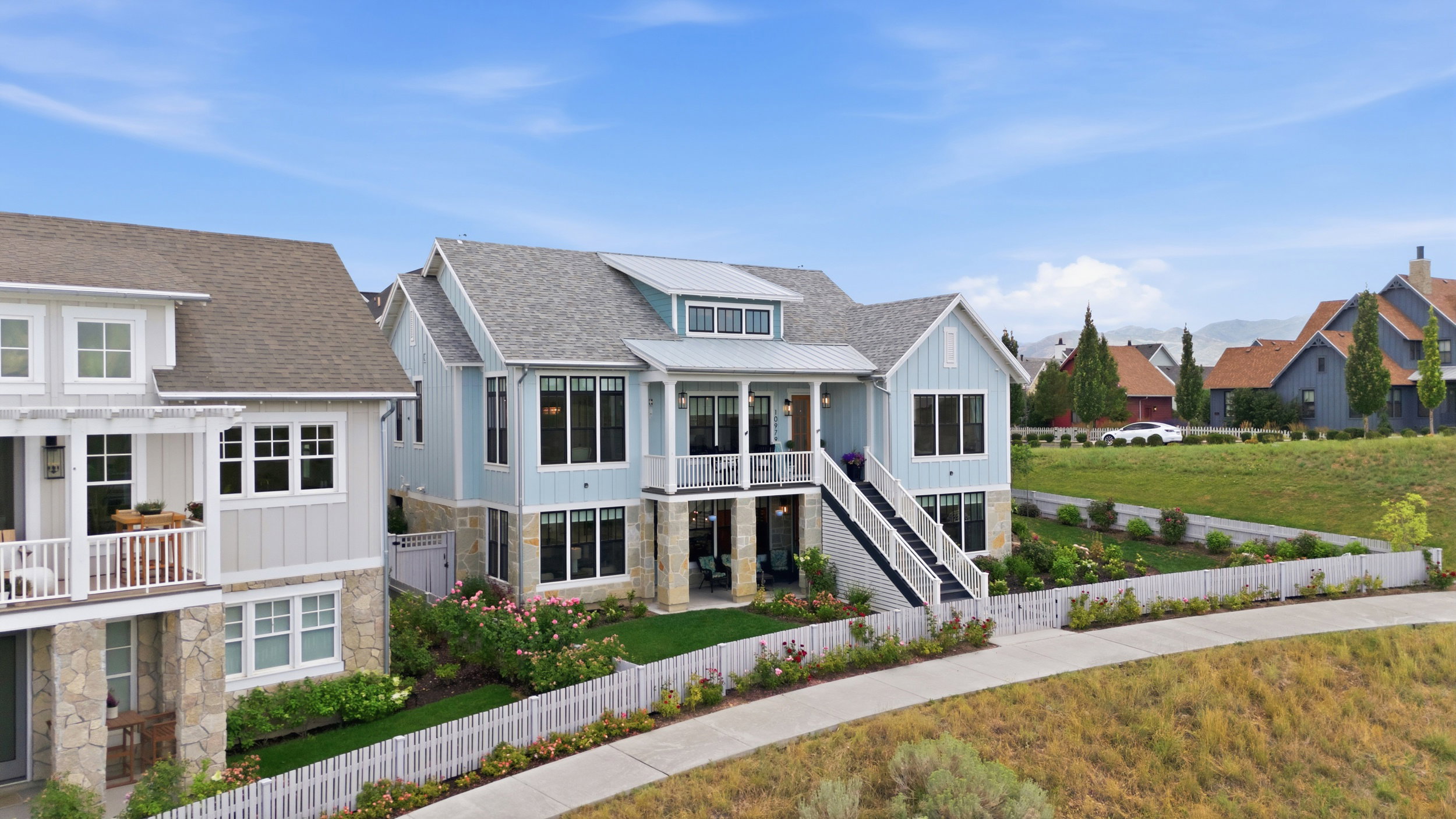 Light blue siding exterior featuring stone accents, a white picket fence, a two-story deck, and a multi-tiered staircase