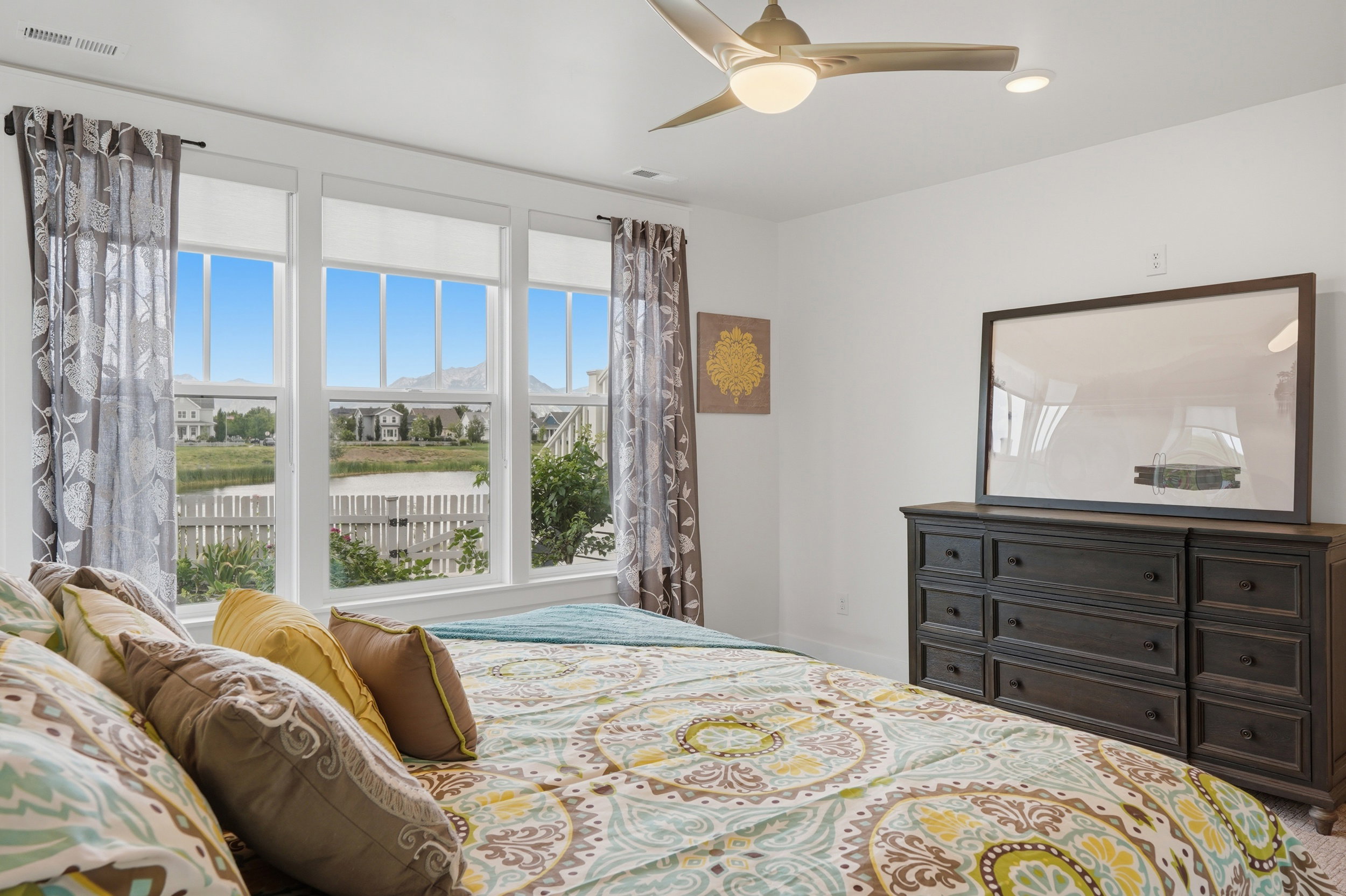 Bright bedroom featuring a multi-pane window array, a contemporary ceiling fan with integrated lighting, recessed lighting, and a dark wood-finish dresser