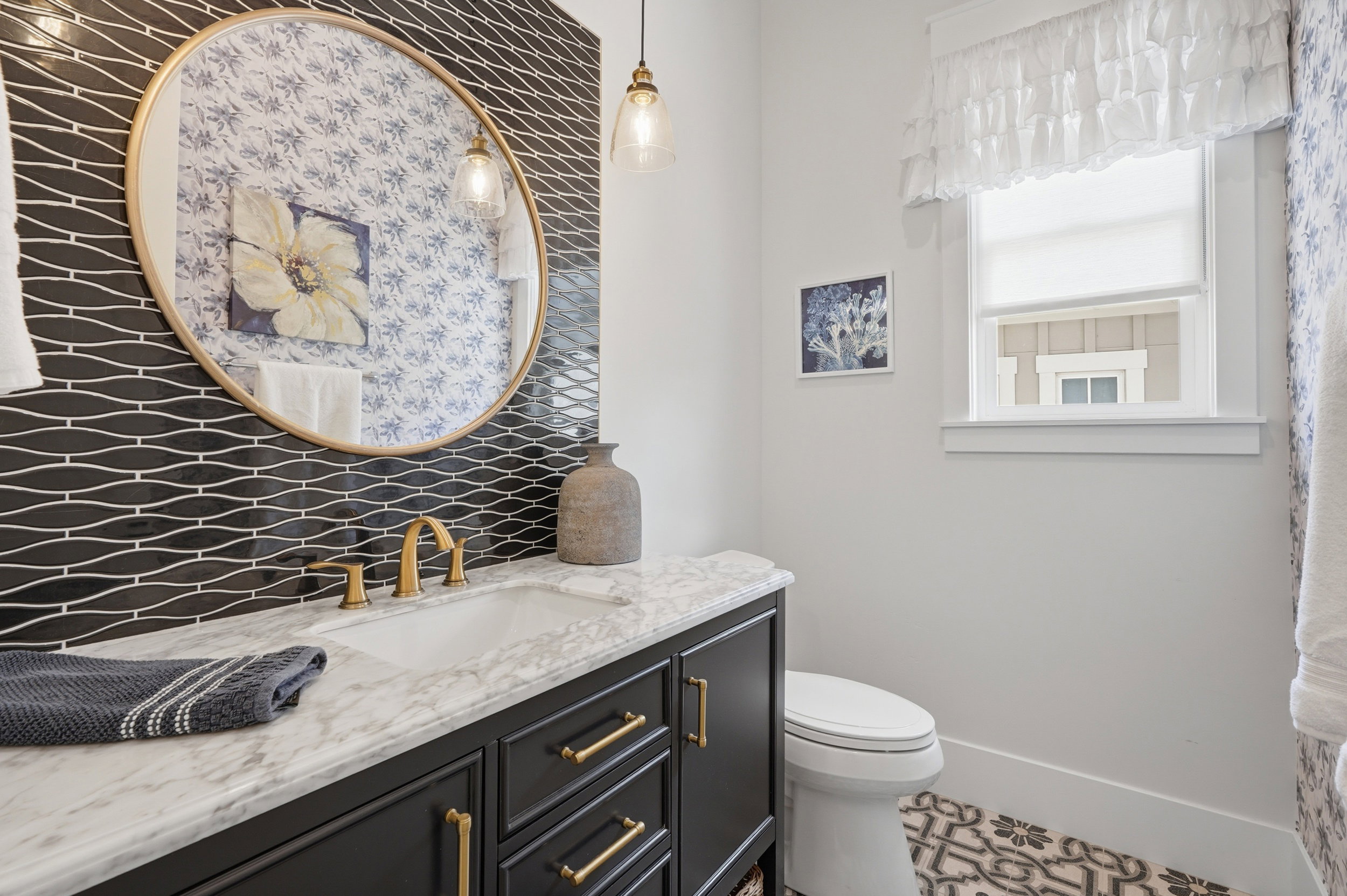 Bathroom vanity featuring a navy blue cabinet with gold hardware, a white marble countertop, and a rectangular undermount sink with a brass faucet