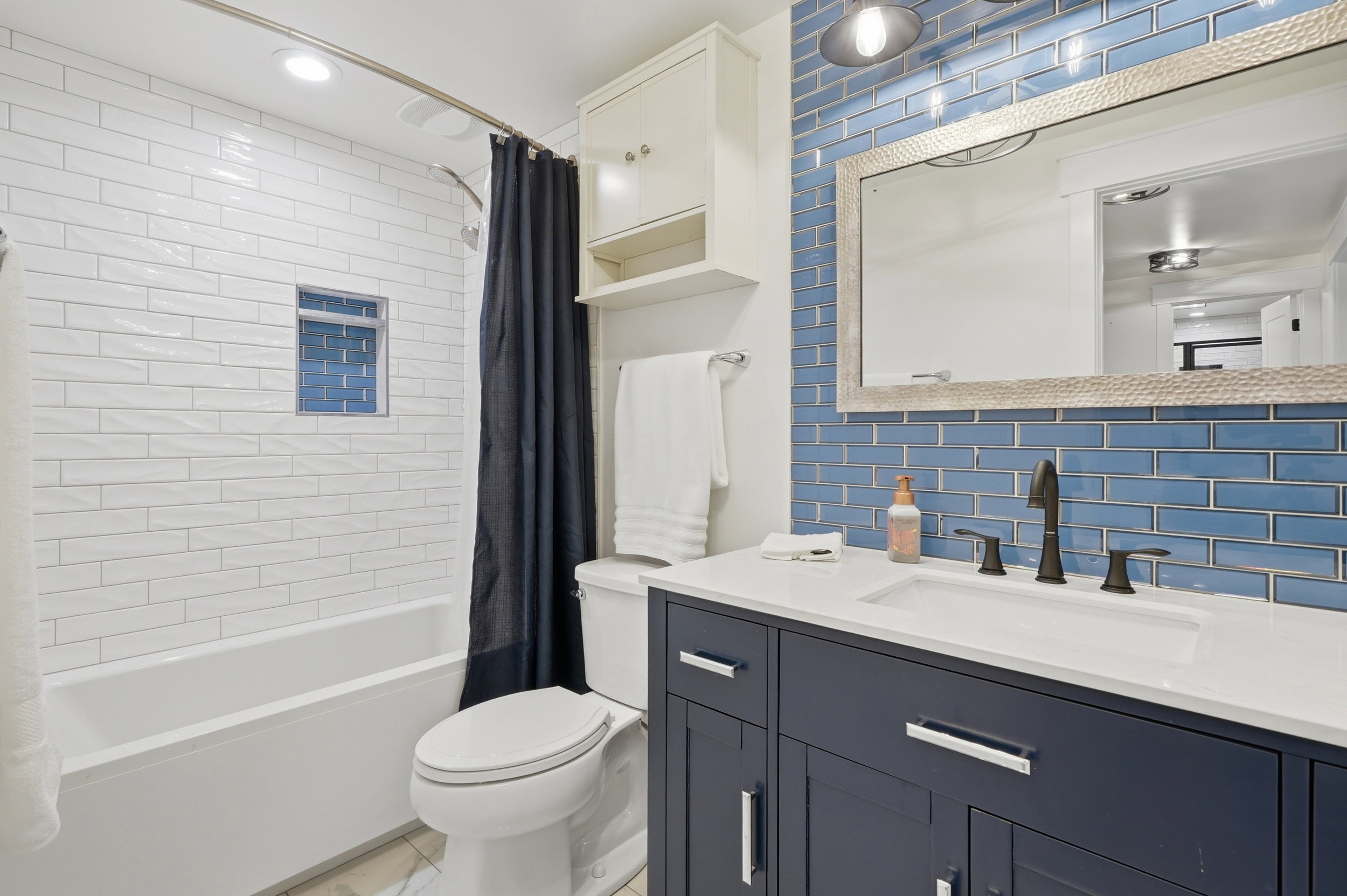 Bathroom featuring a white subway tile shower surround with a tiled niche, a deep blue vanity with a white countertop, and a blue subway tile backsplash