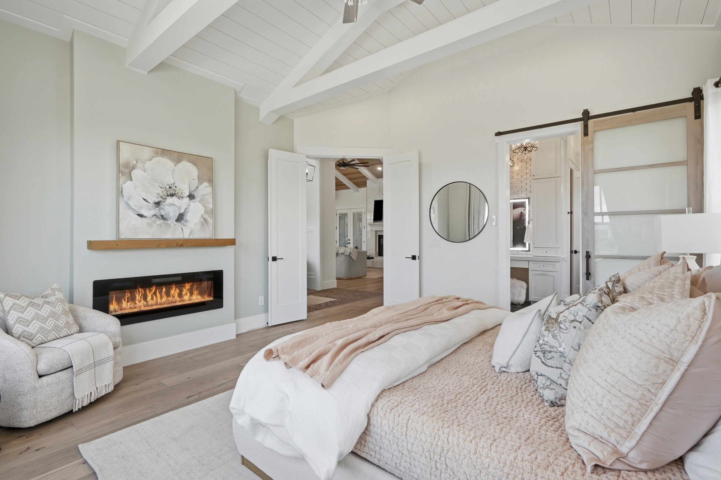 Vaulted ceiling with exposed beams, wood-finish flooring, linear electric fireplace with wood mantel, white paneled doors, and barn door entry