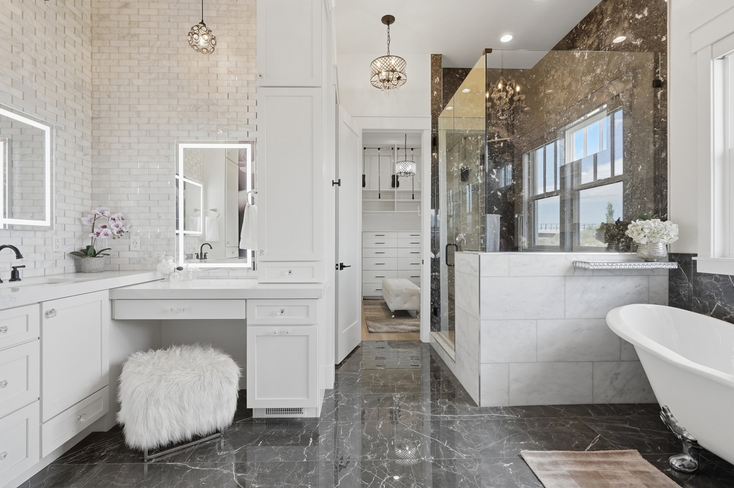 Spacious bathroom featuring dark marble-look flooring, a freestanding clawfoot tub, a walk-in shower with clear glass enclosure, a double vanity with integrated sinks, and white subway tile wall accents