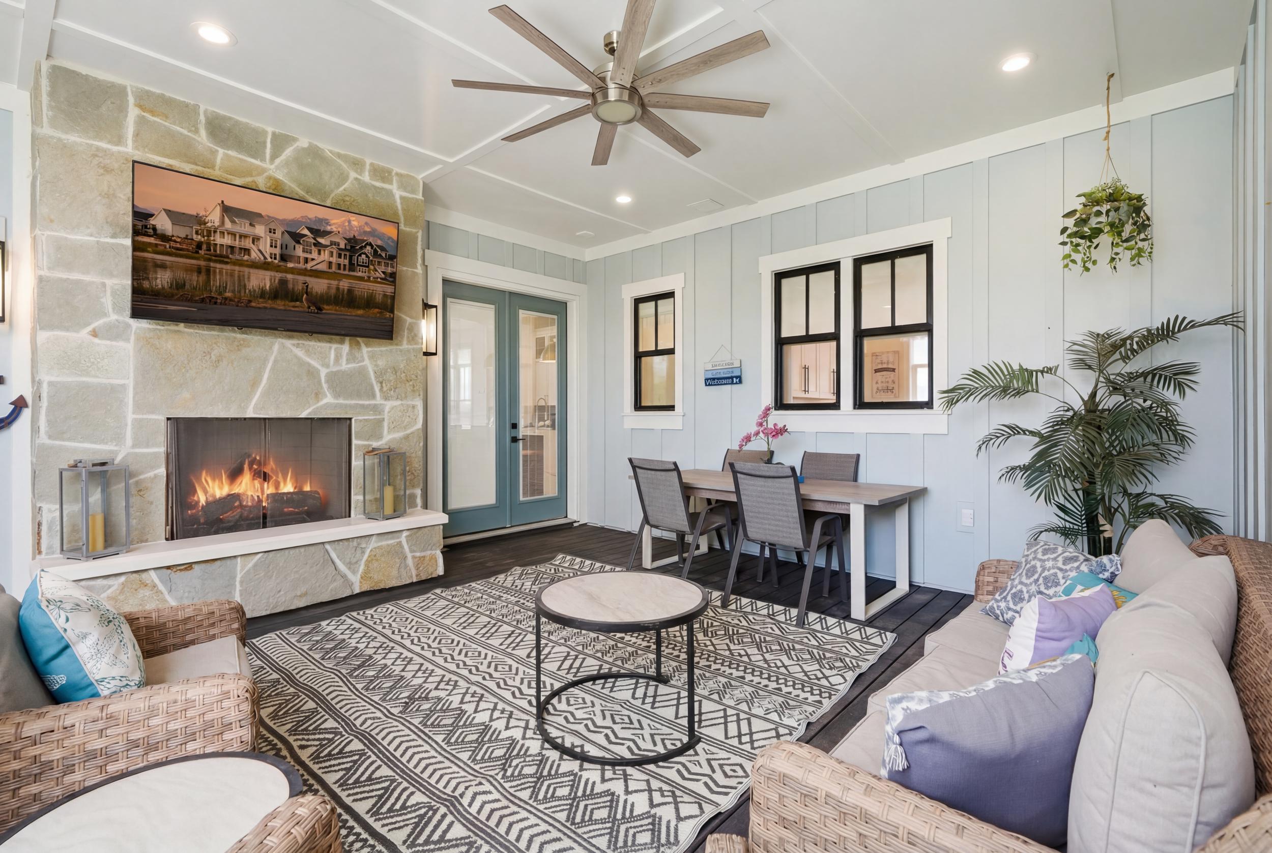 Outdoor living area featuring a stone fireplace with a raised hearth, light blue board and batten wall paneling, and a large ceiling fan