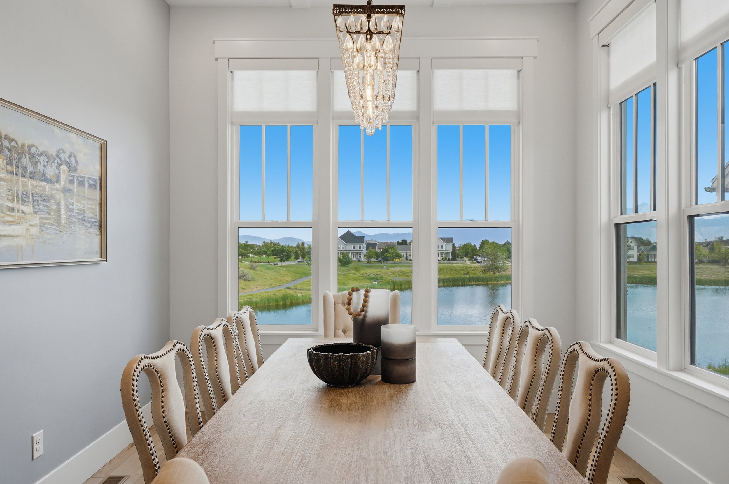 Dining area featuring a prominent crystal chandelier, large windows with white trim, and a serene water feature backdrop
