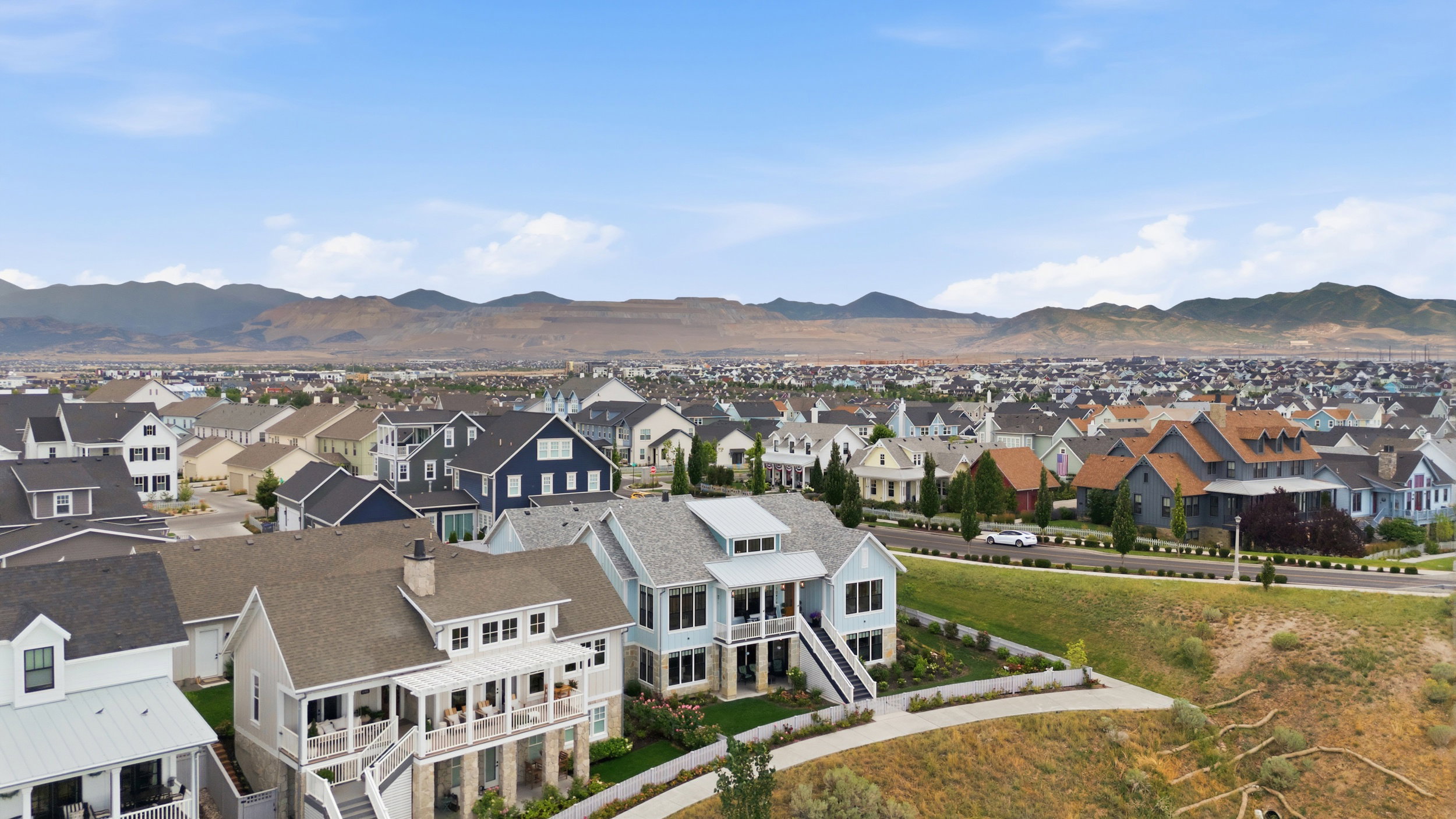 Expansive residential community featuring diverse architectural styles and abundant landscaping, set against a distant mountain range under a clear sky