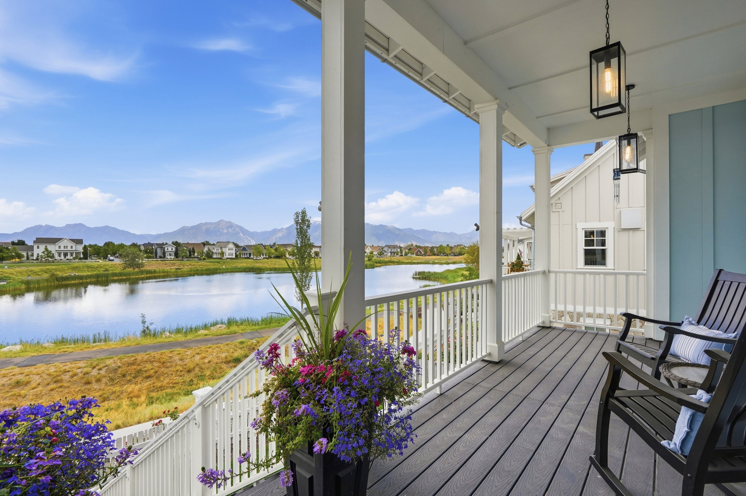 Covered porch with composite decking and white railing overlooking a serene lake and distant mountains