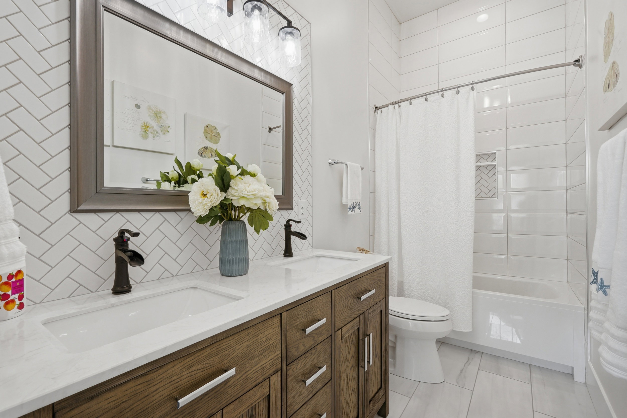 Bathroom featuring a dual vanity with a white countertop and wood-finish cabinetry, herringbone tile backsplash, and a tub-shower combination with a tiled surround