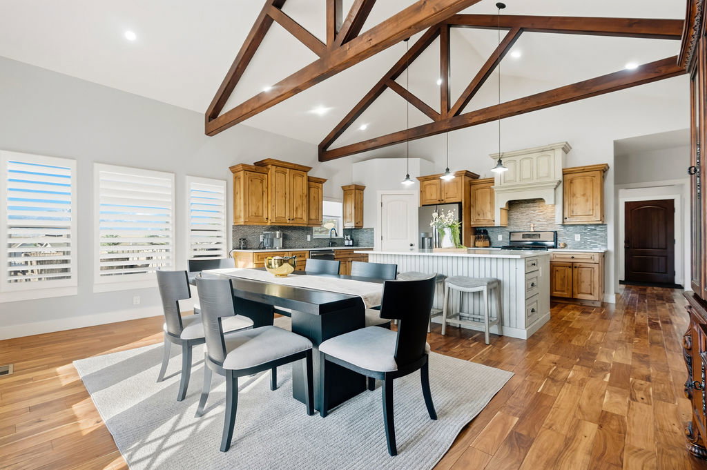 Open-concept living space featuring vaulted ceilings with exposed wood beams, wood-finish flooring, a kitchen island with seating, a patterned tile backsplash, and plantation shutters