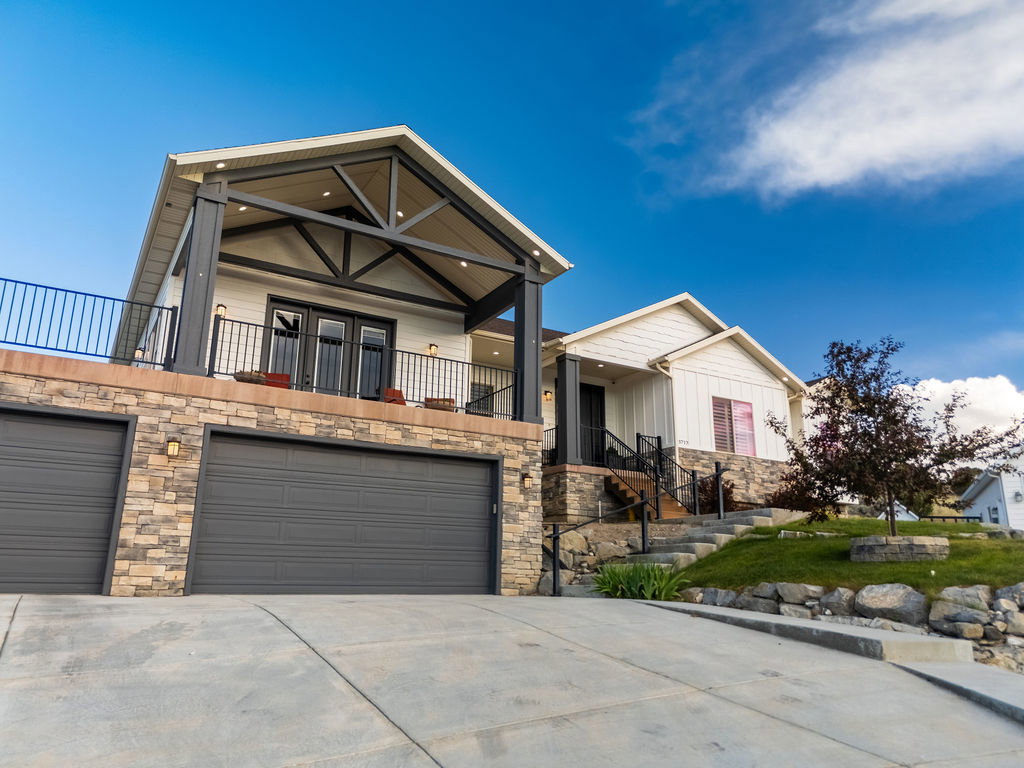 Modern exterior featuring stone veneer siding, multiple garage doors, and an upper-level balcony with black railings