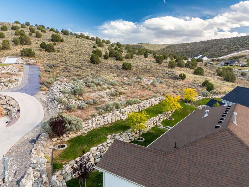 Landscaped property with tiered rock walls, mature greenery, and a paved pathway