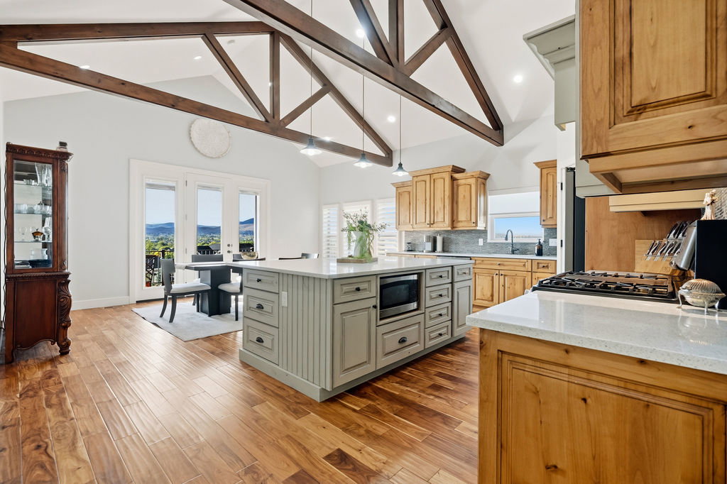 Spacious kitchen featuring a large central island with integrated microwave, wood-finish flooring, exposed beam vaulted ceilings, and extensive cabinetry