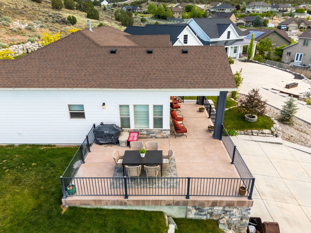 Expansive concrete patio featuring a partial overhead covering, black metal railings, and stone-clad retaining wall
