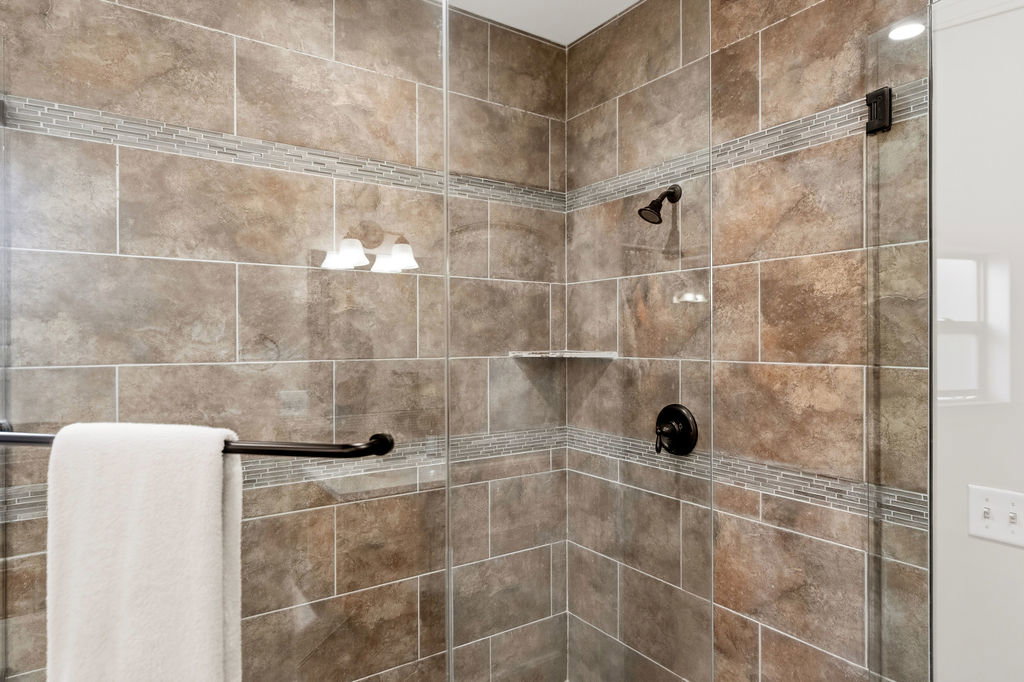 Shower enclosure with large format tiled walls, mosaic tile accent bands, oil-rubbed bronze fixtures, and a glass panel surround