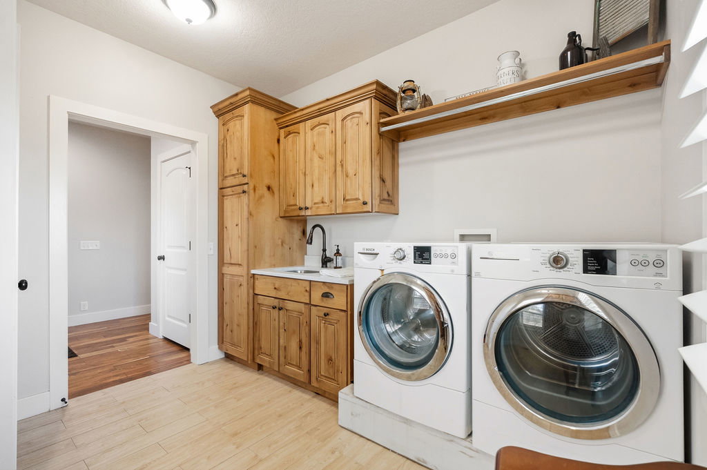 Dedicated laundry area featuring light wood-finish cabinetry, a single basin sink with a matte black faucet, and a light wood-finish floating shelf with an integrated hanging rod