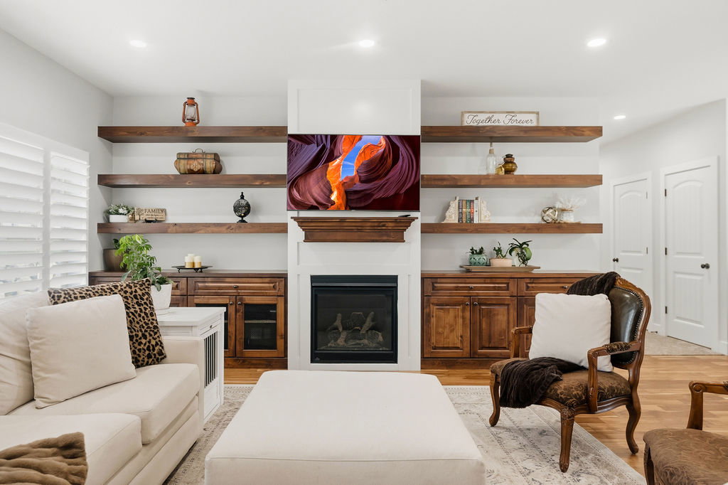 Living area featuring a central fireplace with a mantel, flanked by built-in cabinetry and open wood-finish shelving