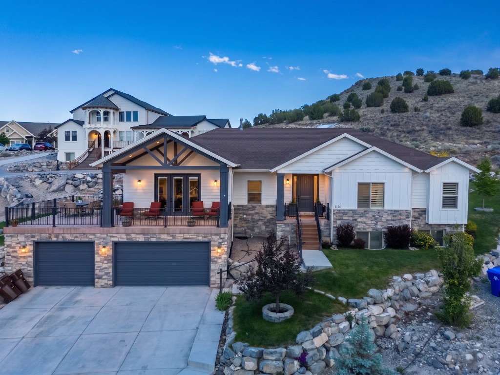 Contemporary exterior featuring white siding, stone veneer accents, an expansive upper-level deck, a covered entryway, and an attached two-car garage