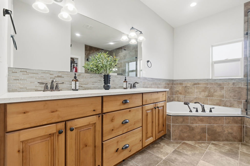 Bathroom featuring a spacious double vanity with wood cabinetry, light-colored countertops, and a full-width mirror