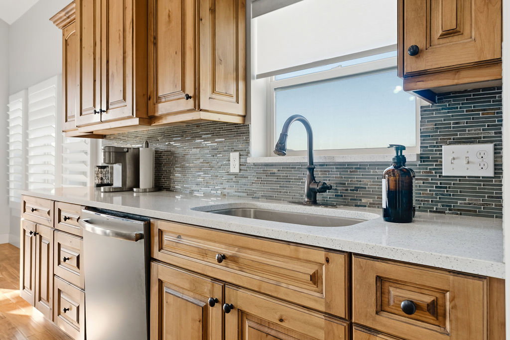 Kitchen featuring wood-finish cabinetry, light-toned countertops, a stainless-steel sink, and a dark-finish gooseneck faucet