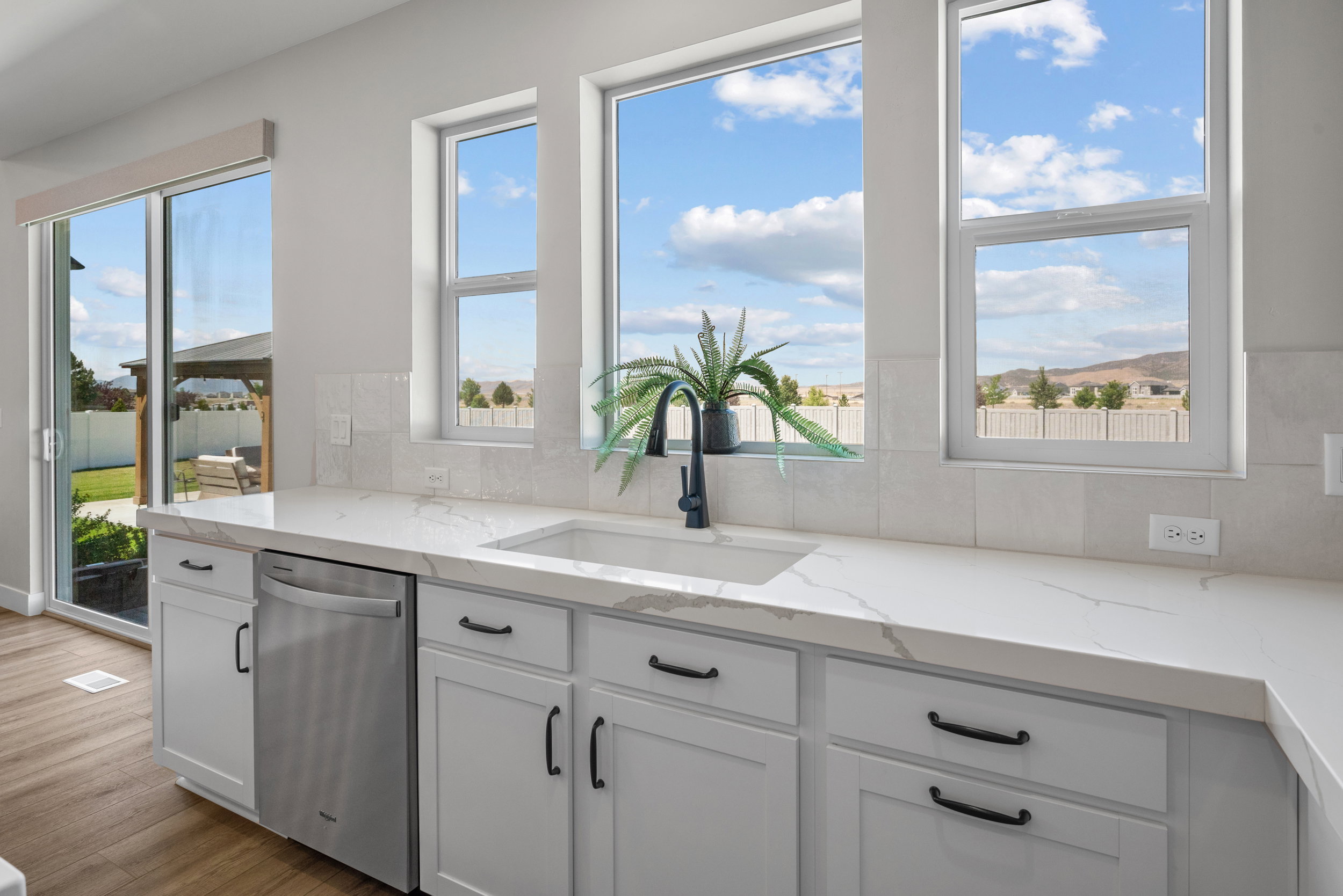 Kitchen sink area featuring a white undermount sink, a matte black gooseneck faucet, and a stone-finish countertop with subtle veining