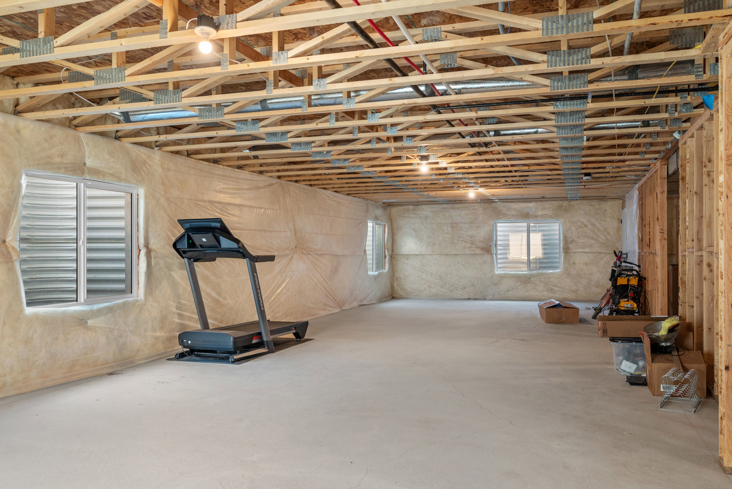 Unfinished basement featuring exposed wood joists, concrete flooring, multiple egress windows, and framed wall sections