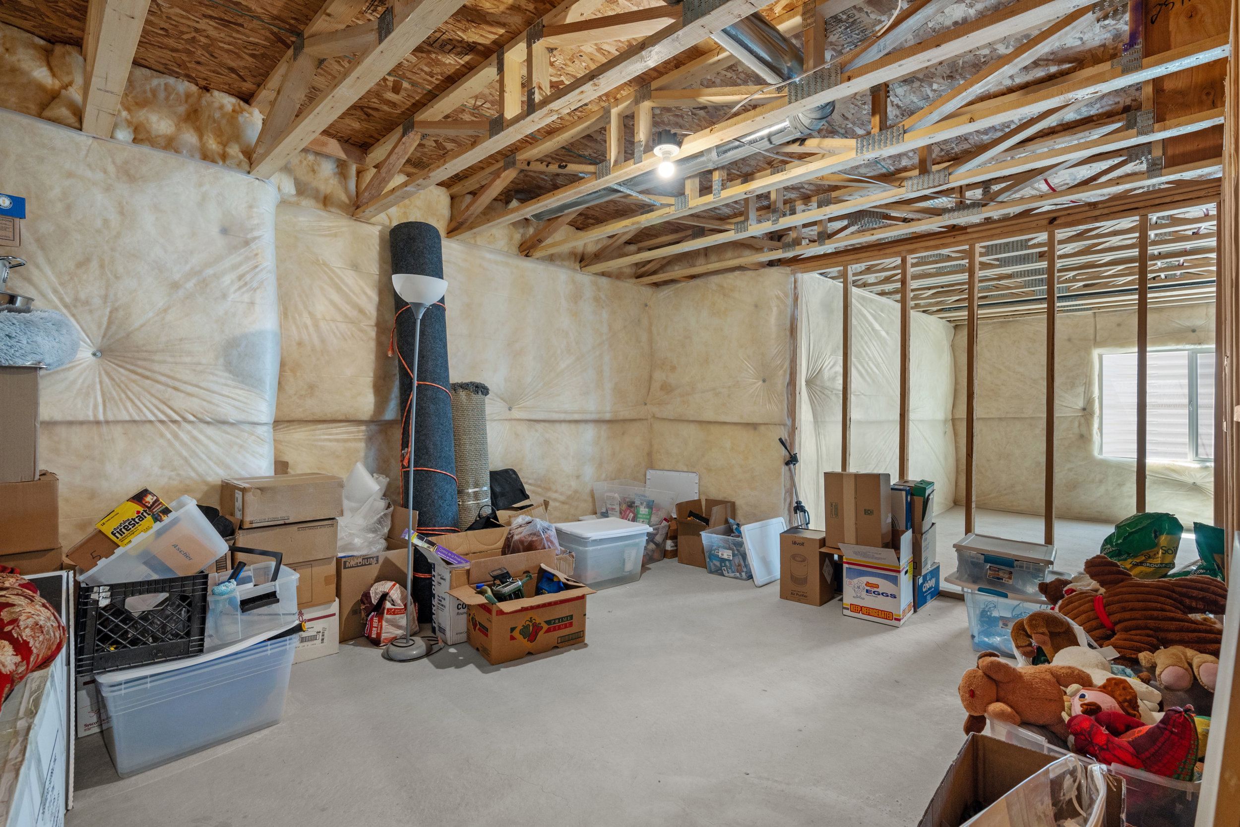 Unfinished basement with exposed ceiling joists and support beams, featuring insulation-wrapped walls and a concrete floor