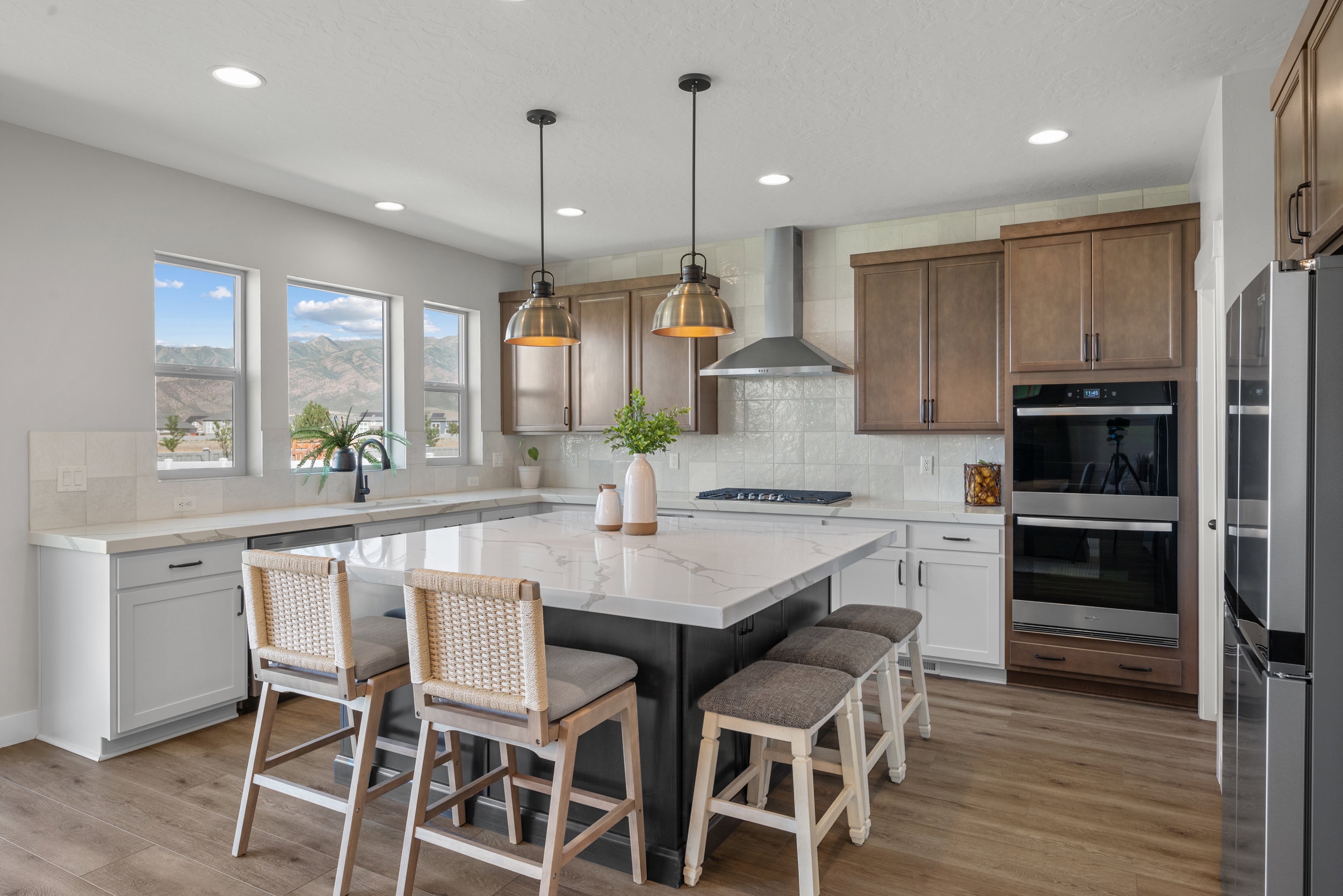 Spacious kitchen featuring a large central island with seating, a stainless steel range hood, double wall ovens, built-in refrigerator, and wood-finish flooring