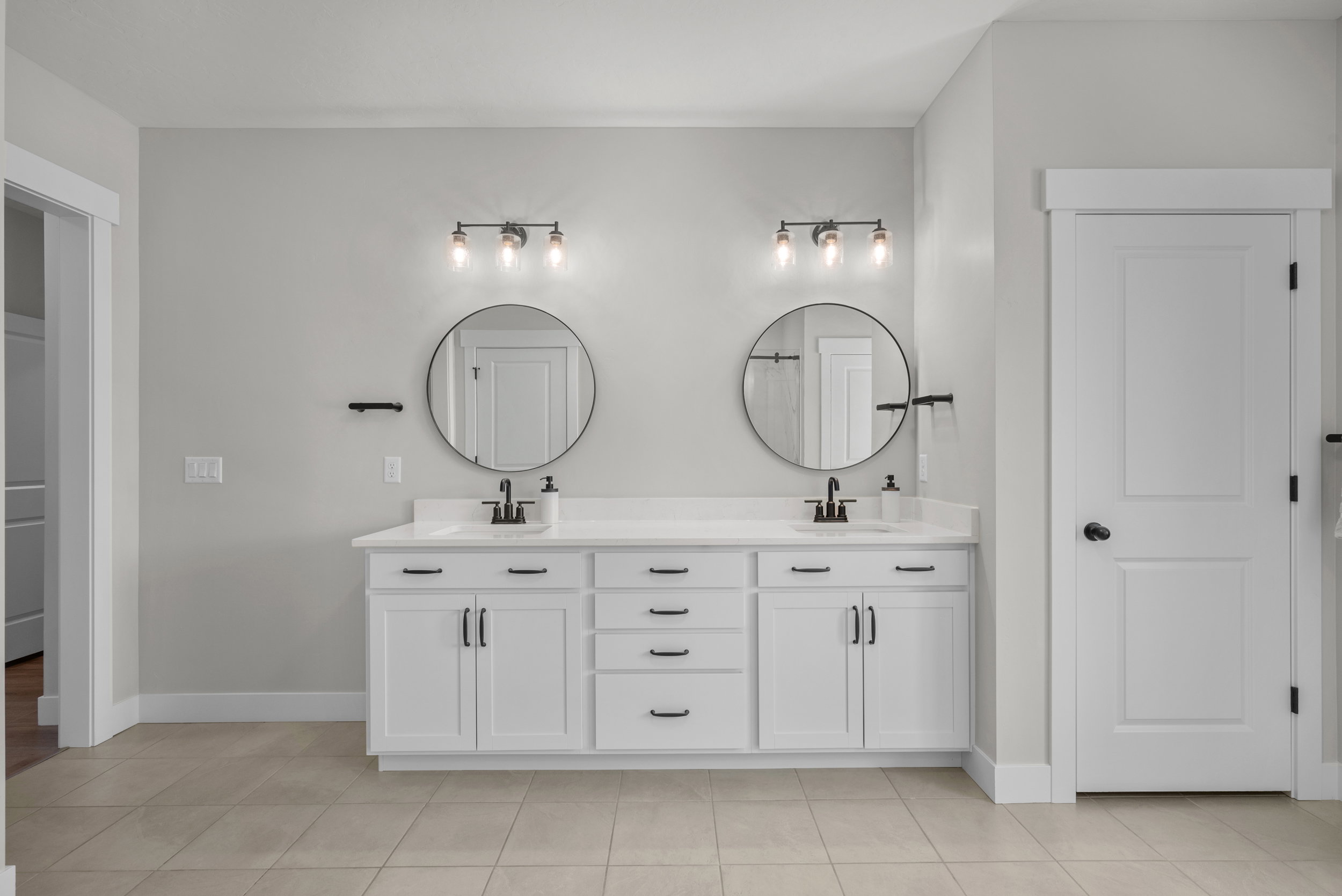 Double vanity featuring white cabinetry with matte black hardware, dual undermount sinks, and a light-toned countertop