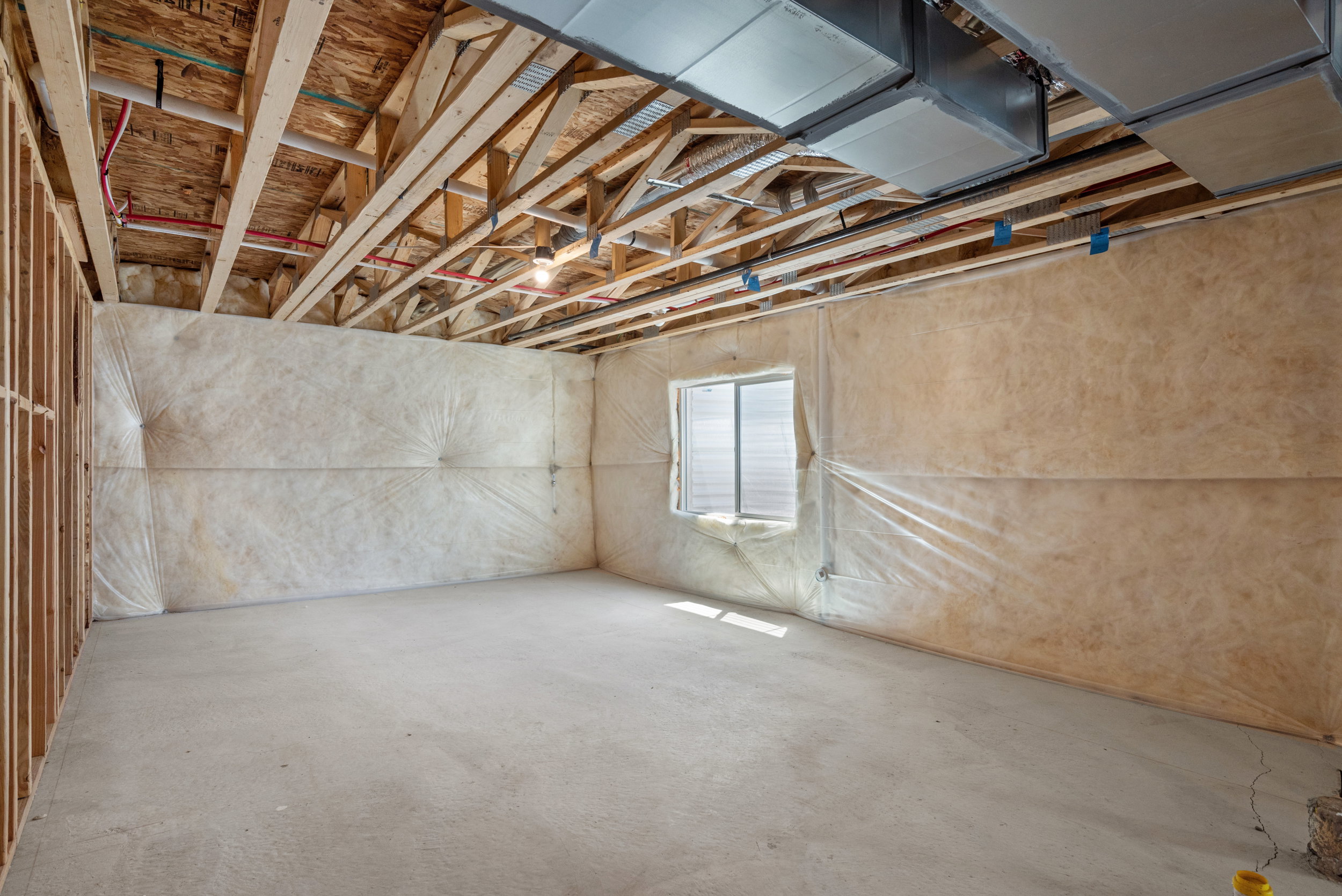 Unfinished basement featuring exposed wood joists, concrete flooring, and insulated walls