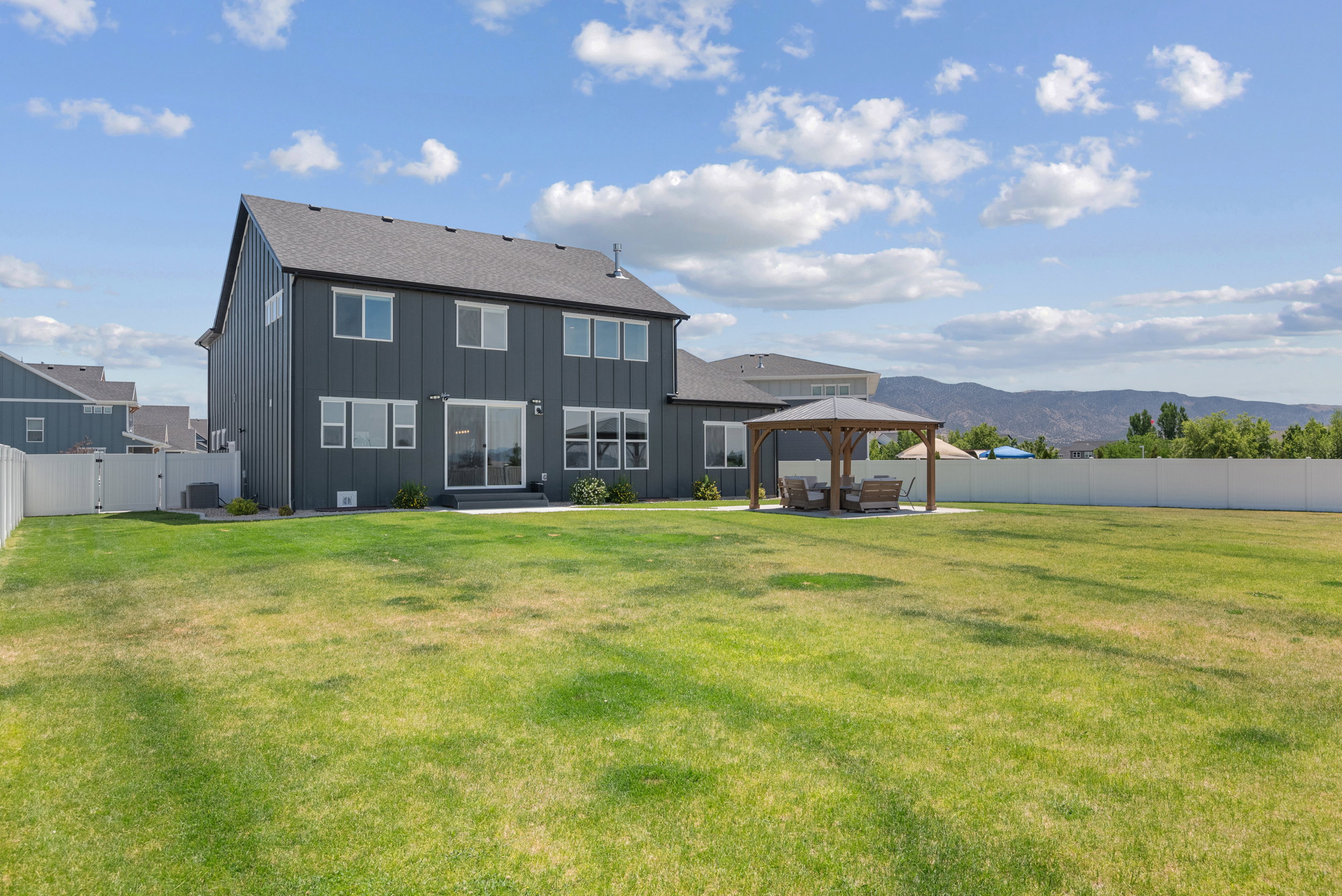 Expansive backyard featuring a gazebo with a concrete pad, a white privacy fence, and mountain scenery
