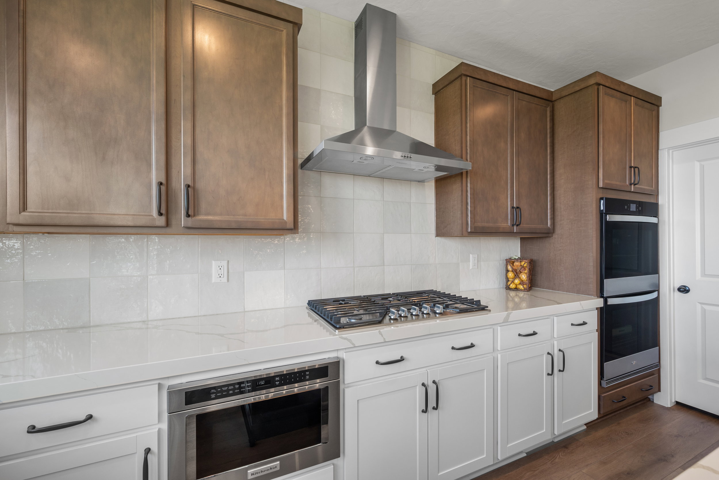 Modern kitchen featuring two-tone cabinetry, a stainless steel range hood, and white countertops