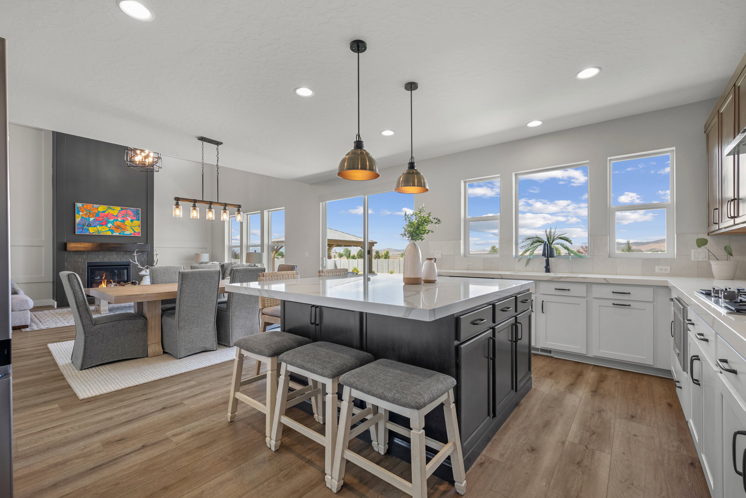 Open-concept living space with a large kitchen island, wood-finish flooring, recessed lighting, and a fireplace with a dark accent wall