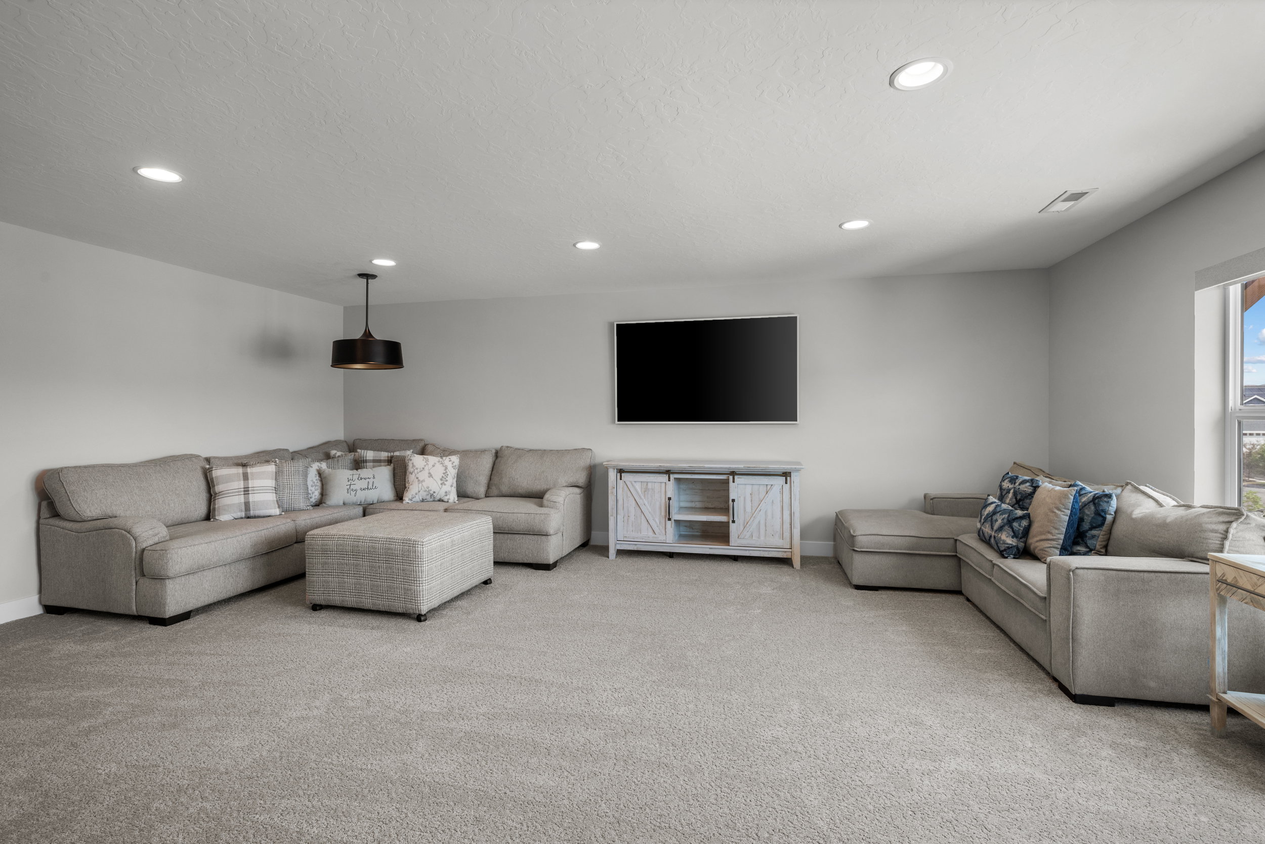 Spacious carpeted room featuring recessed lighting, a ceiling-mounted pendant light, and a window providing natural illumination