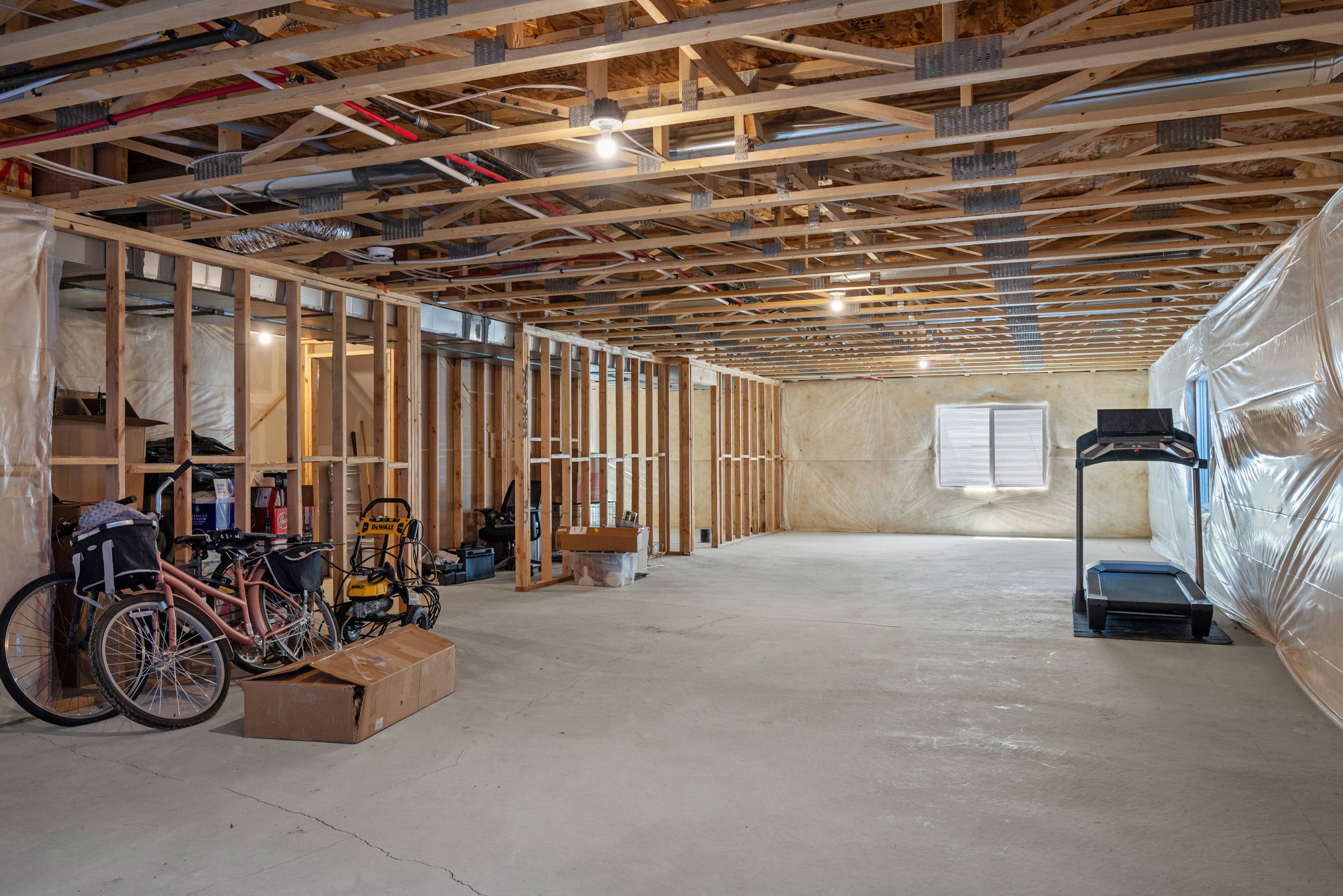 Unfinished basement featuring exposed wood joists, concrete flooring, framed interior walls, and visible utility lines
