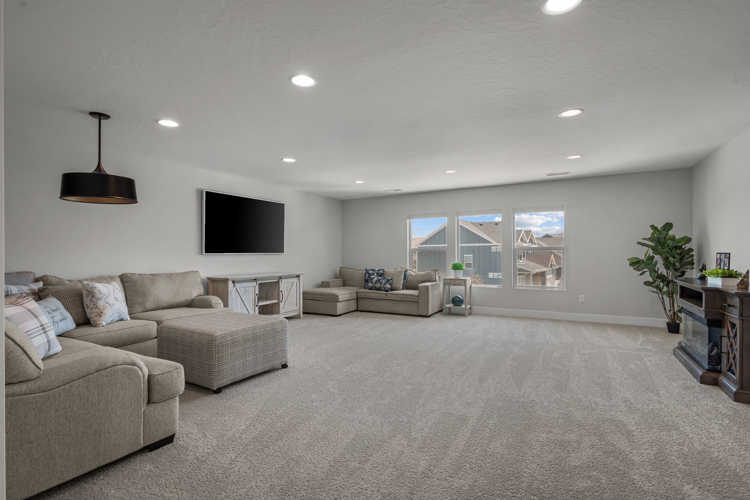 Spacious living area featuring light gray walls, recessed lighting, and a large triple window array