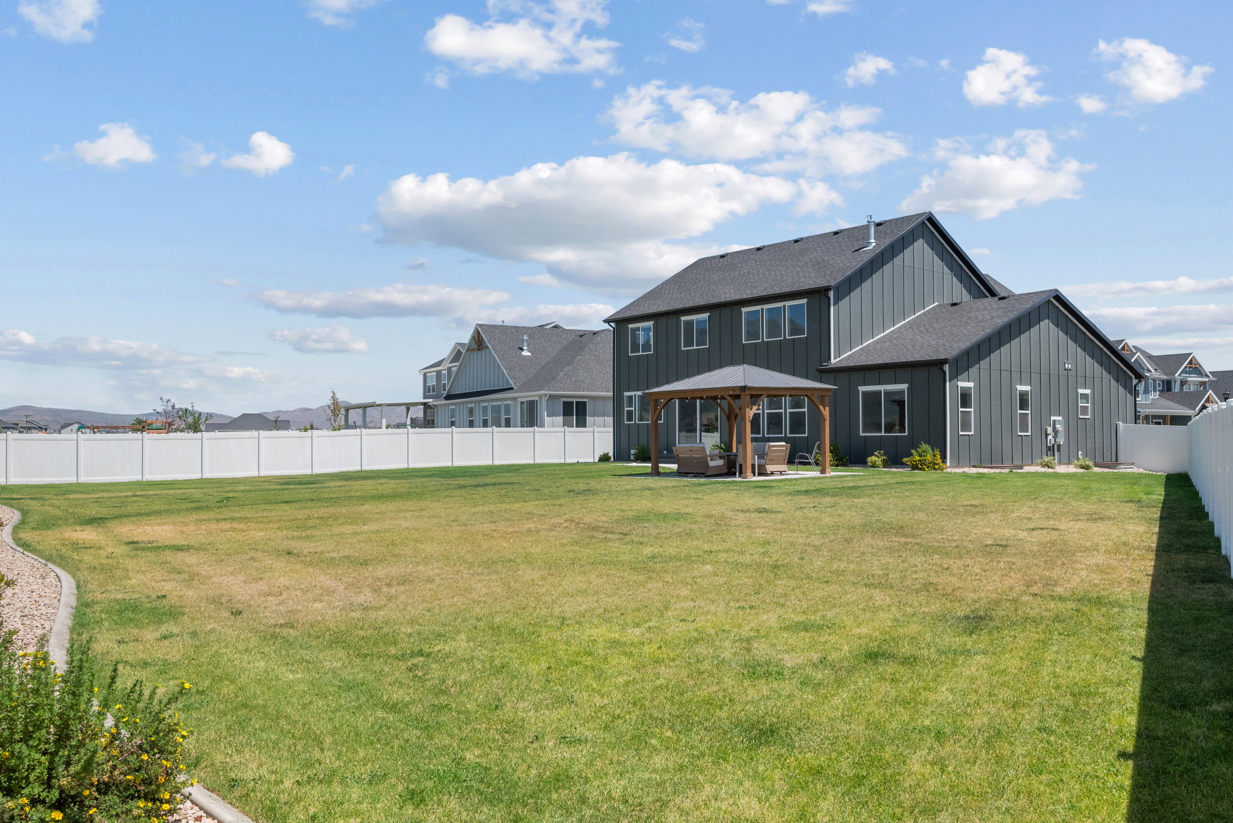 Expansive backyard featuring a large green lawn, full vinyl fencing, and a permanent wooden gazebo with a concrete pad
