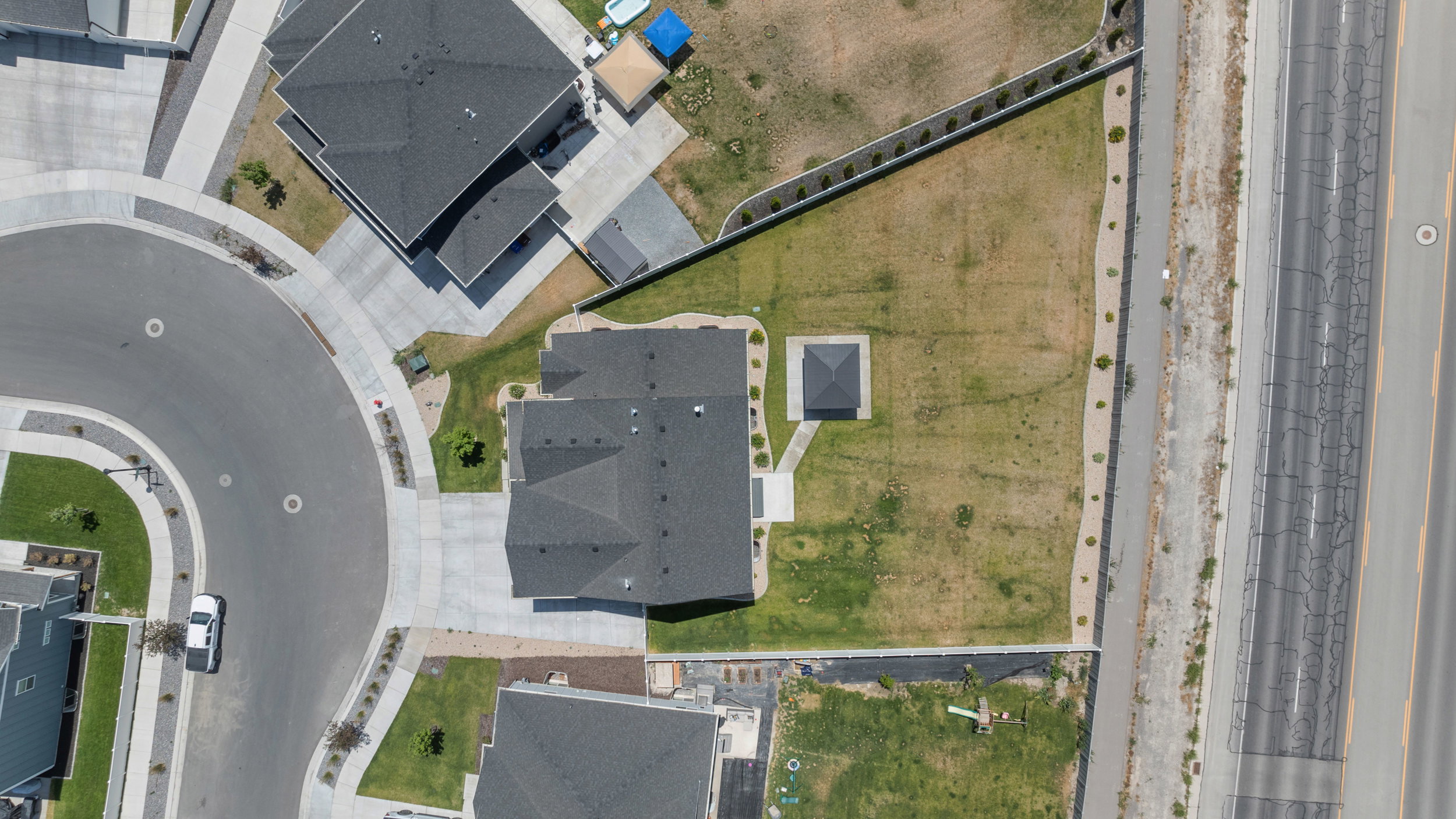 Aerial perspective of a single-family home featuring a dark shingle roof, concrete driveway, and an expansive yard