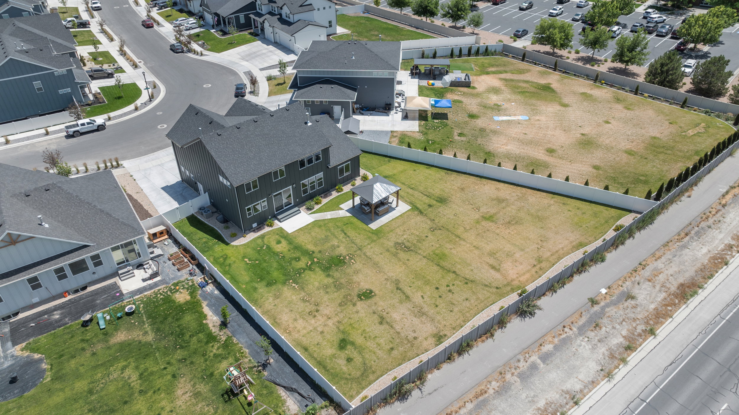 Expansive property featuring a large two-story residence with dark siding and a prominent roofline, a spacious backyard with a gazebo, a concrete patio, and a paved driveway leading to a two-car garage