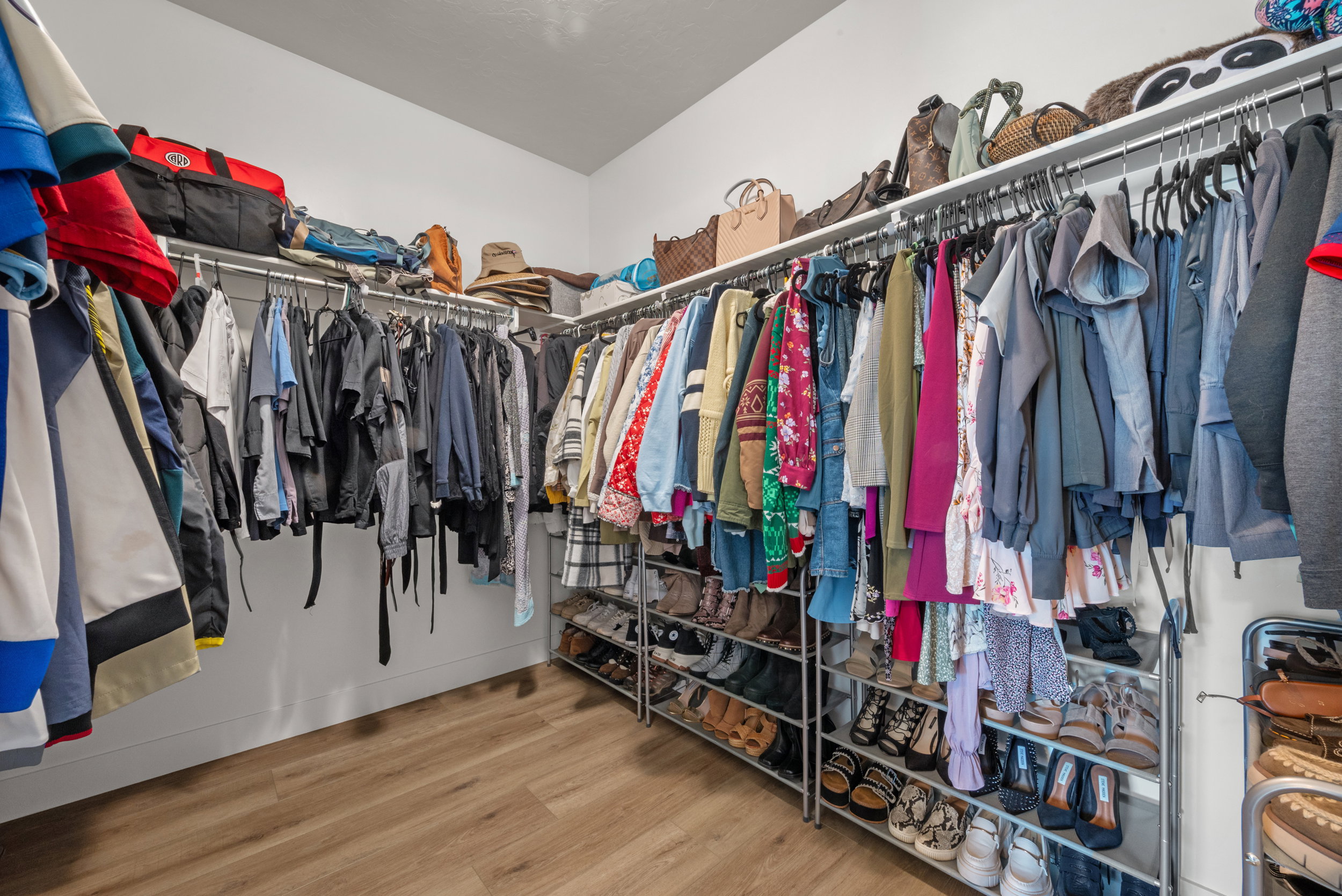 Spacious walk-in closet featuring wood-finish flooring, white walls, and built-in closet organization systems with ample hanging space and shelving