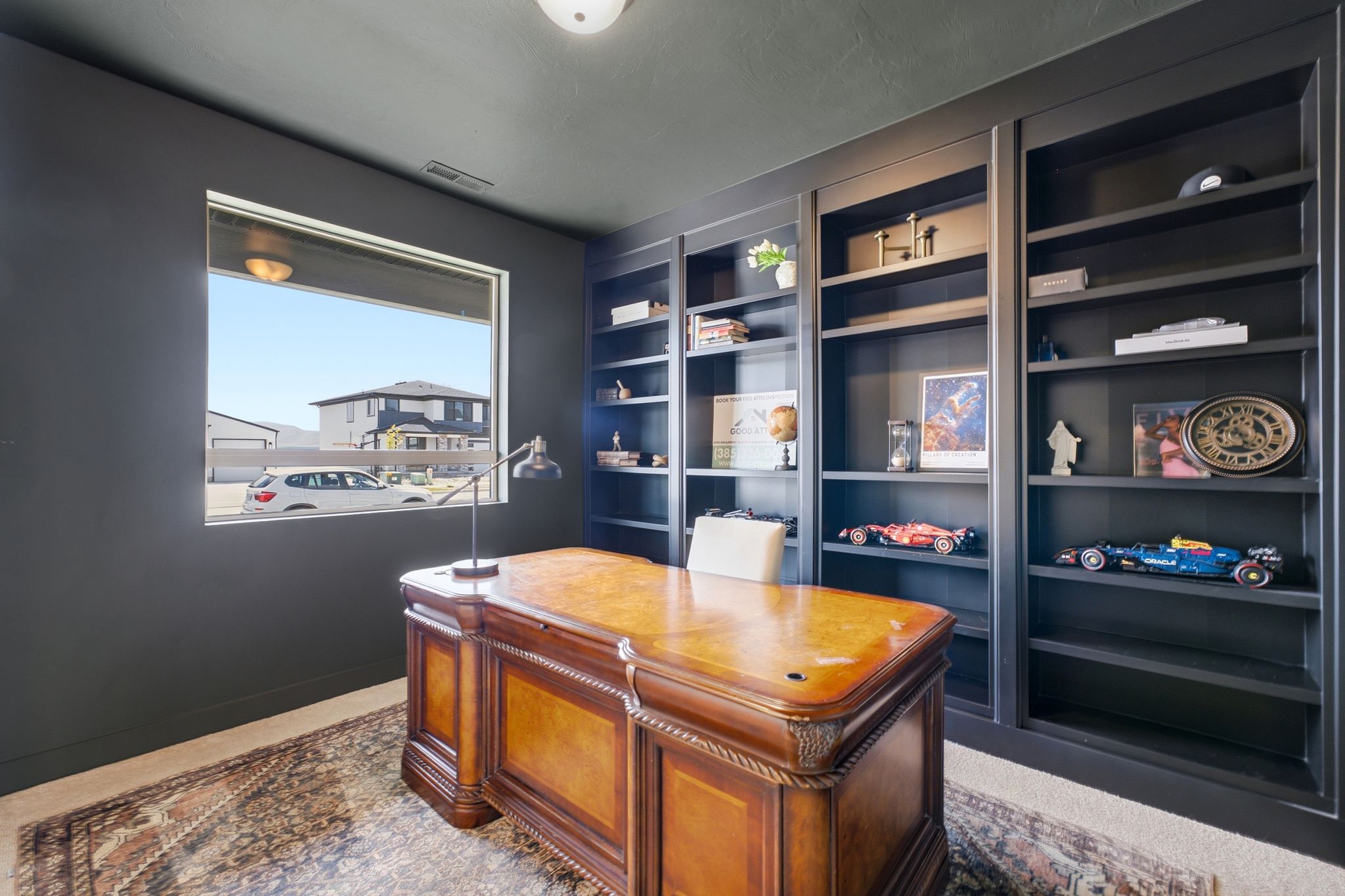 Dedicated office space featuring built-in shelving, a large window, a ceiling-mounted light fixture, dark wall paint, and carpeted flooring