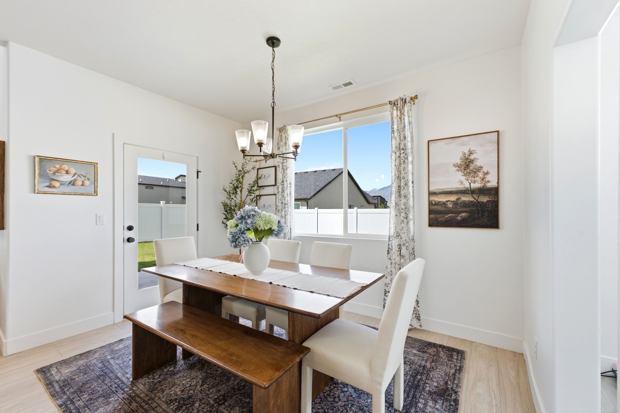 Bright dining area featuring light wood-finish flooring, a contemporary chandelier, a large window, a glass-paned door, and white baseboards