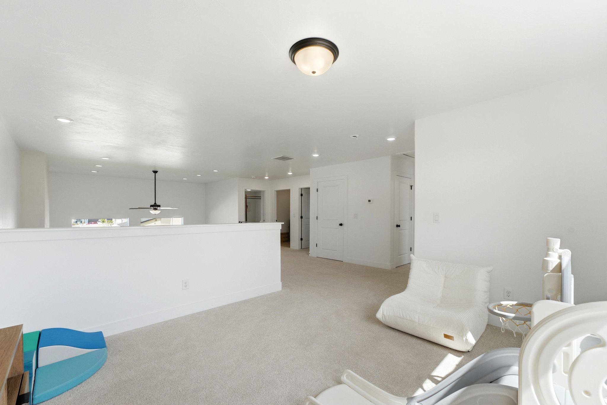 Expansive loft area featuring neutral carpeting, white walls, recessed lighting, and a ceiling fan
