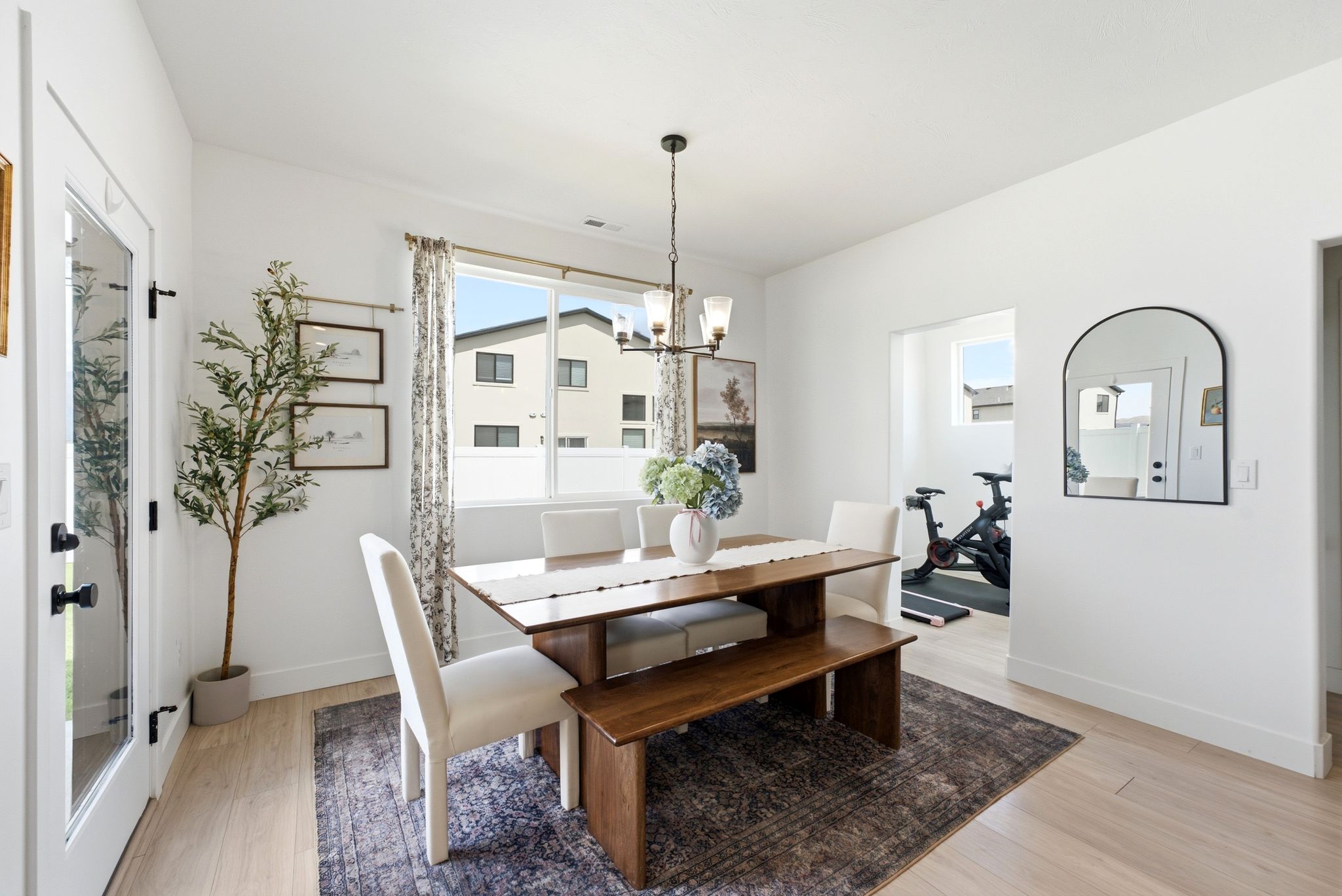 Bright dining area featuring light wood-finish flooring, a contemporary chandelier, and a large window with privacy blinds