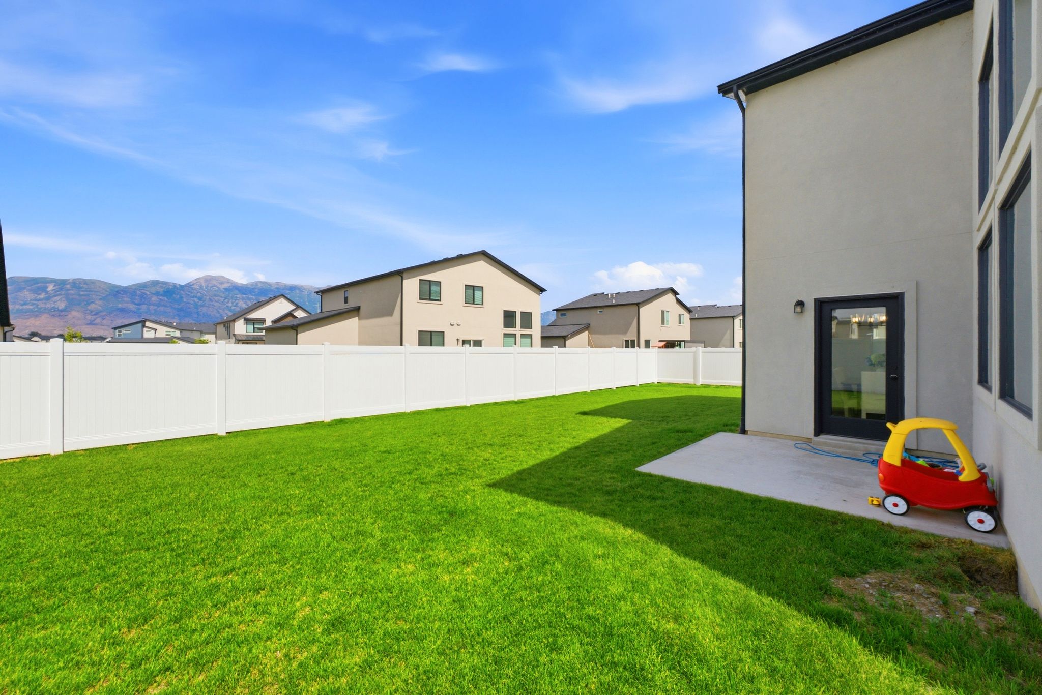 Expansive green lawn with a white privacy fence and a concrete patio