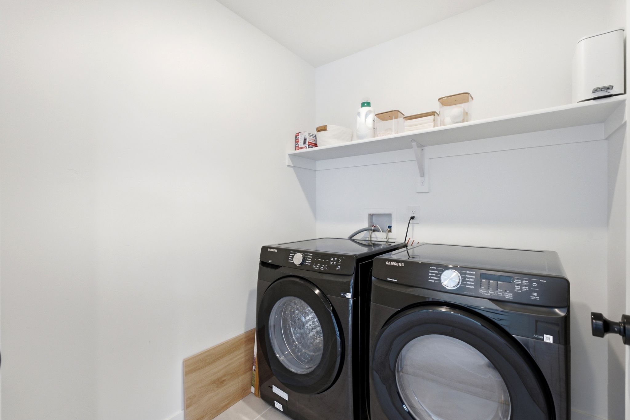Dedicated utility area featuring white walls, a single floating shelf, and wood-finish flooring
