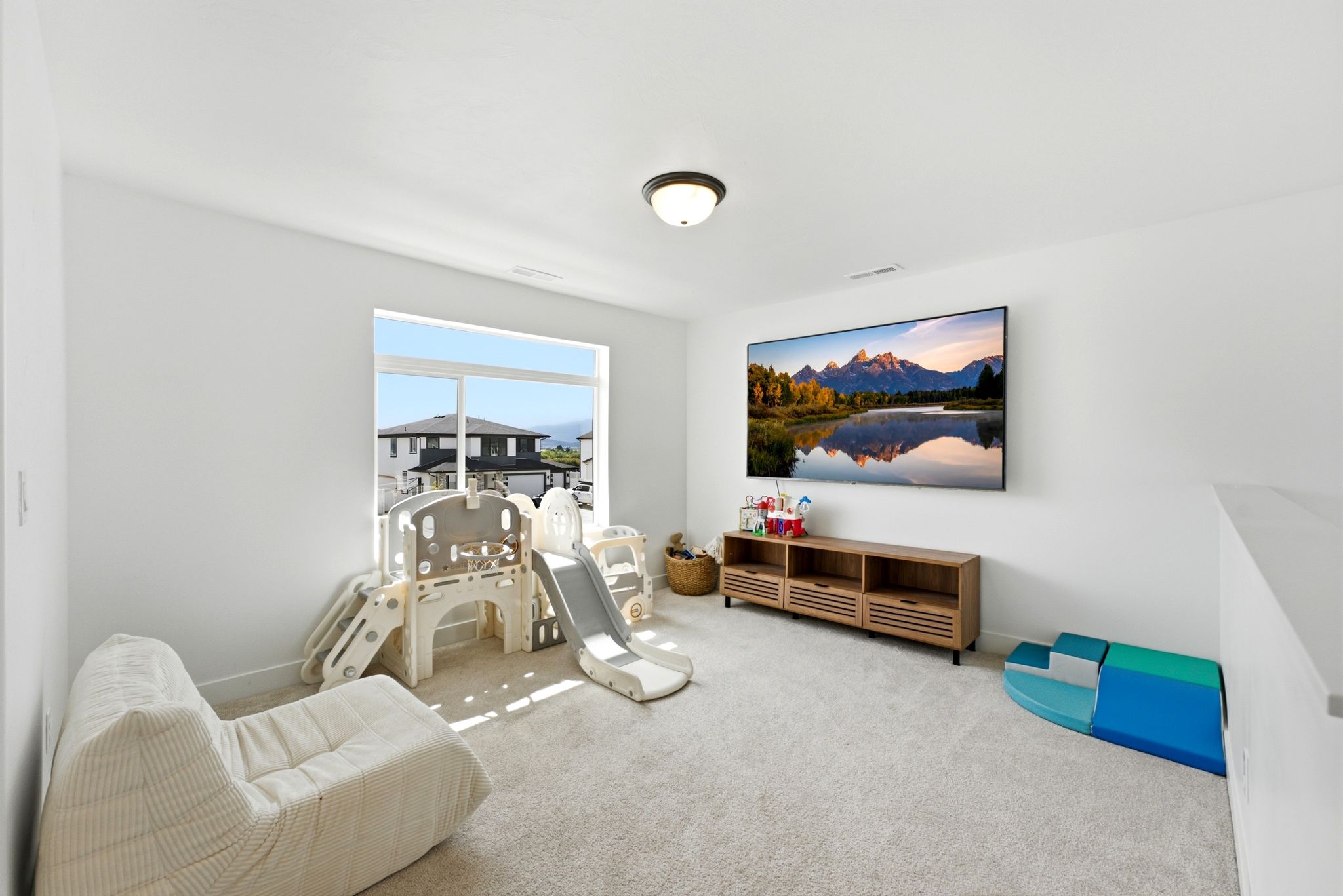 Carpeted room featuring a large window, a wall-mounted television, a wooden media console, and a contemporary ceiling light fixture