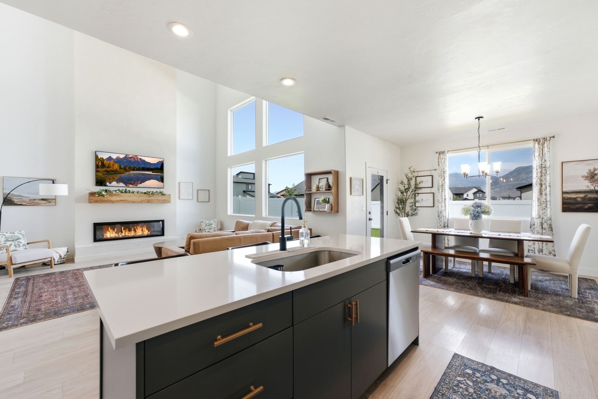 Open-concept living space with a kitchen island featuring a stainless steel sink, a built-in dishwasher, and dark cabinetry with brass hardware