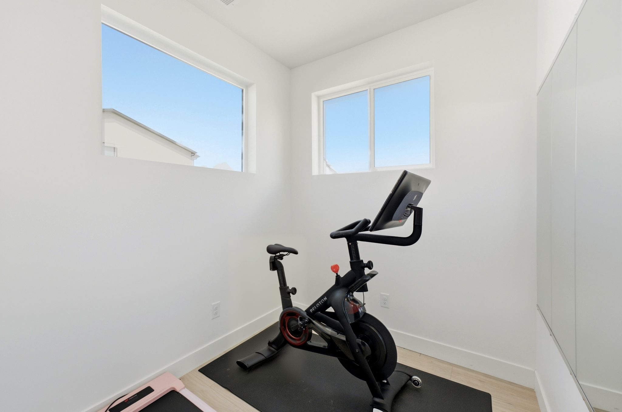 Bright interior space featuring light wood-finish flooring, white walls, and two horizontal windows providing ample natural light