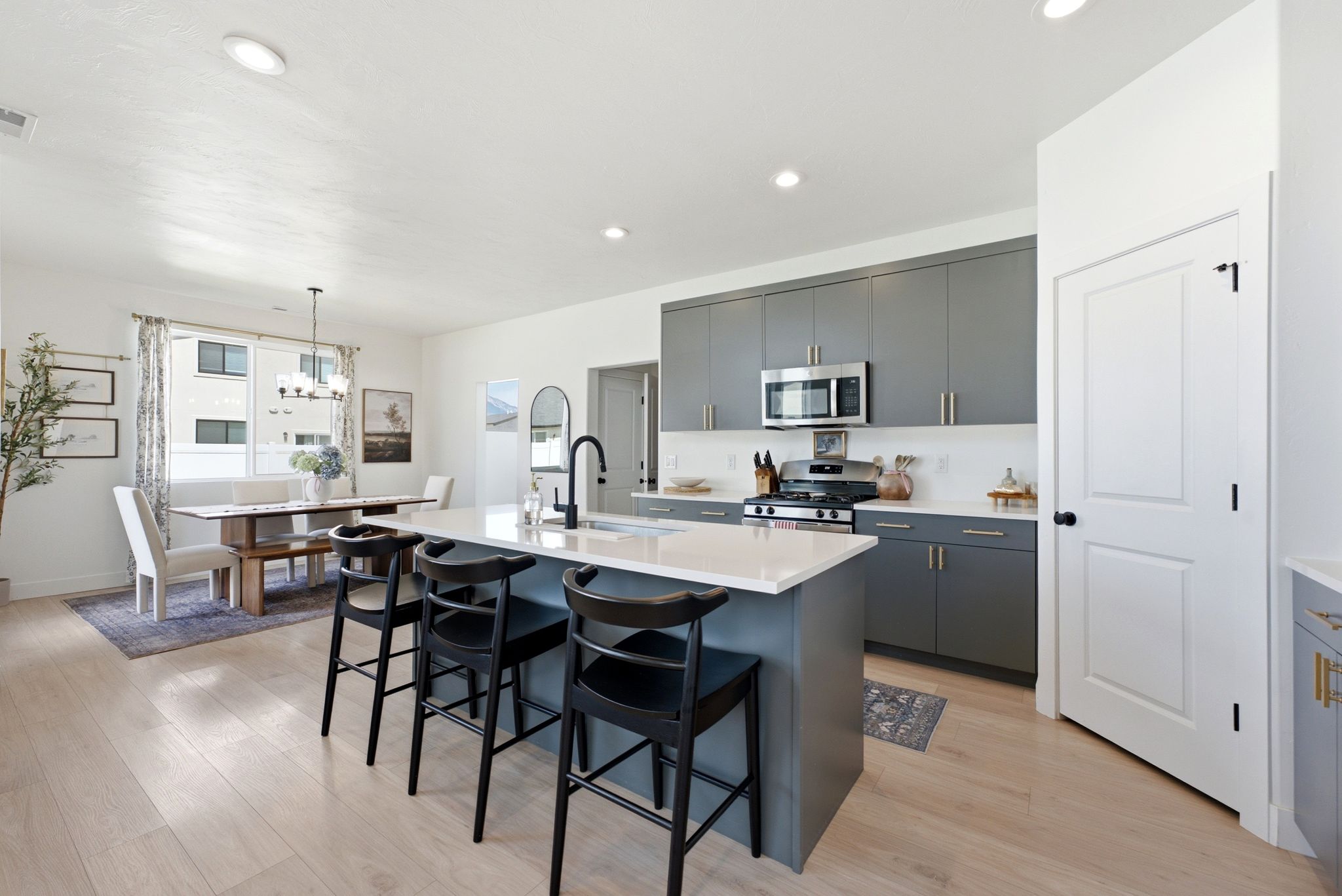 Modern kitchen featuring an island with a light-toned countertop, sleek gray cabinetry, stainless steel appliances, and wood-finish flooring
