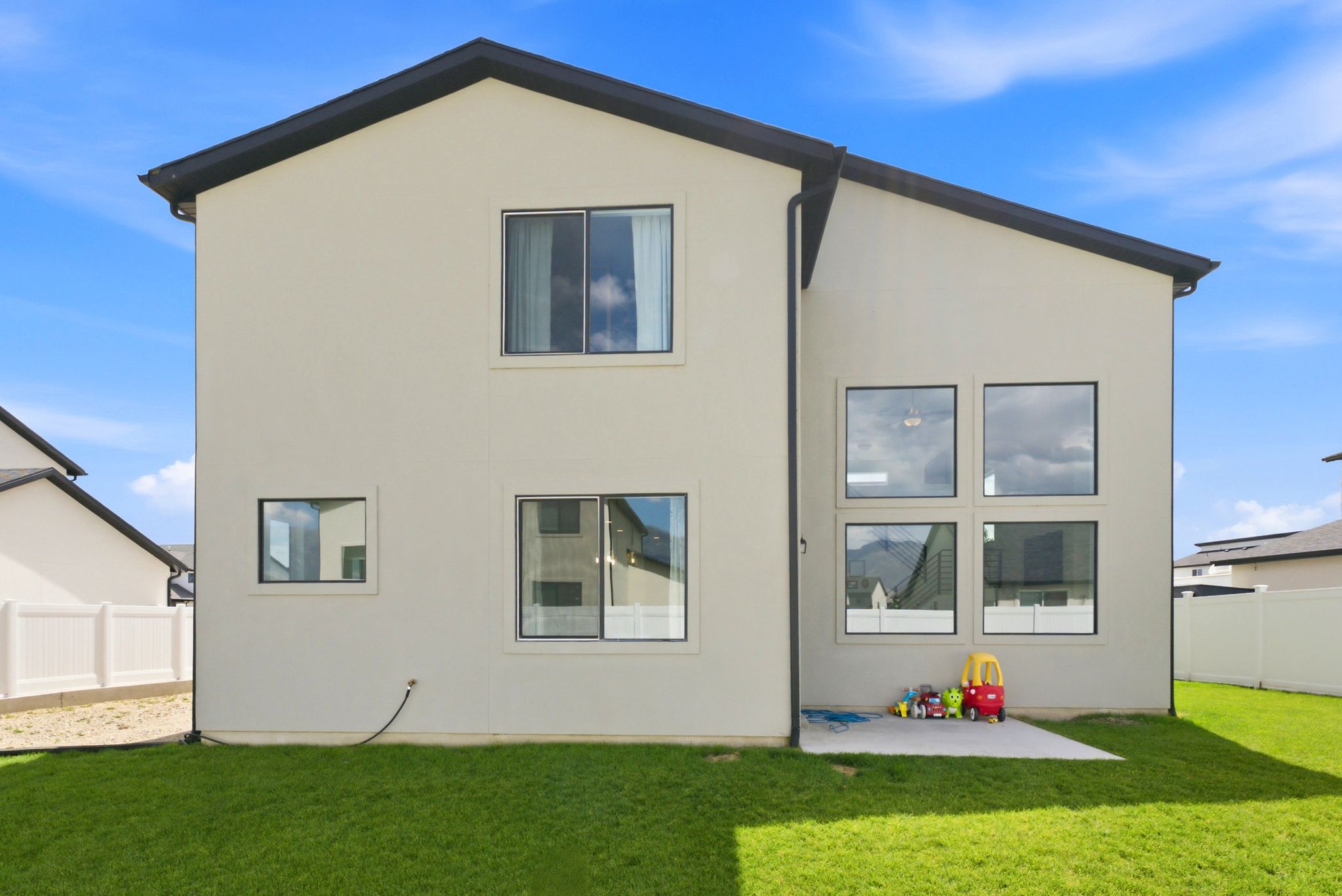 Rear exterior featuring a large grassy area, light-colored stucco siding, and a black roof