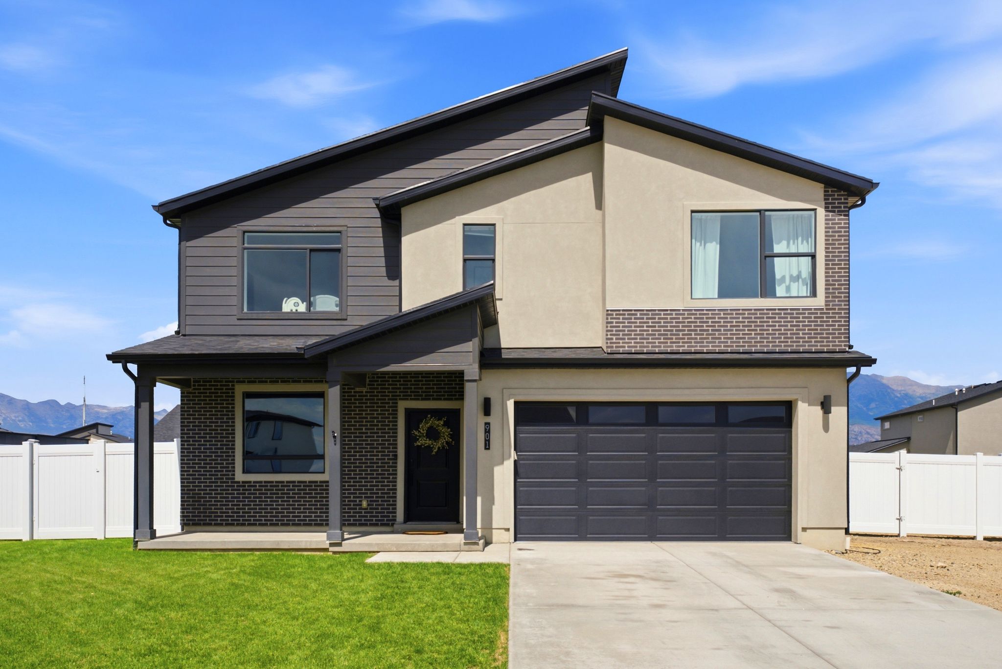 Modern exterior featuring a dark gray garage door, covered entry, and mixed material facade with horizontal siding, stucco, and brick accents